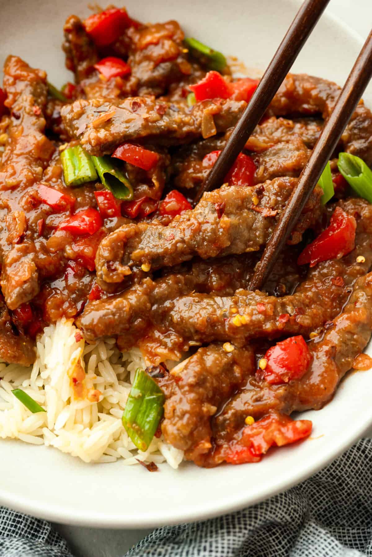 Close view of chopsticks lifting up Beijing beef from a bowl.