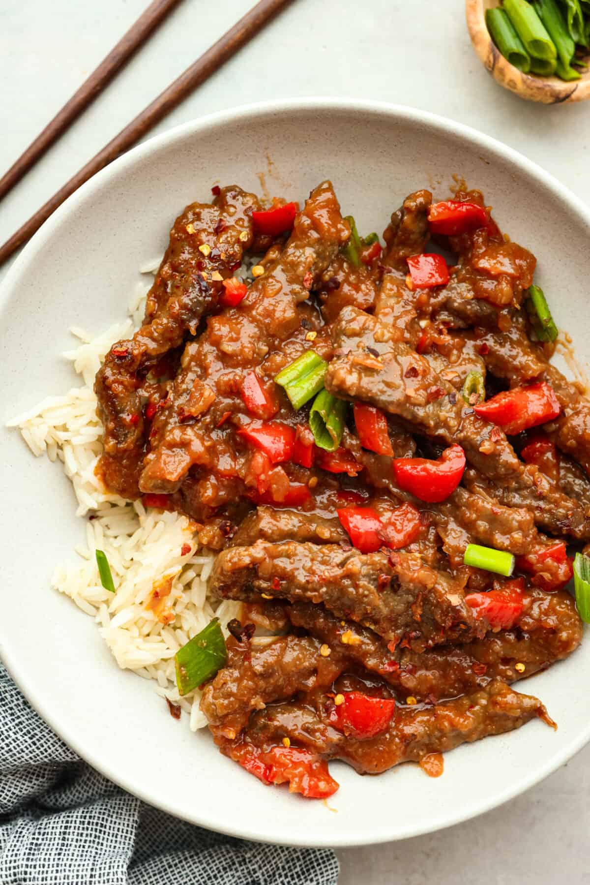 Top view of Beijing beef in a white bowl over rice garnished with green onions.