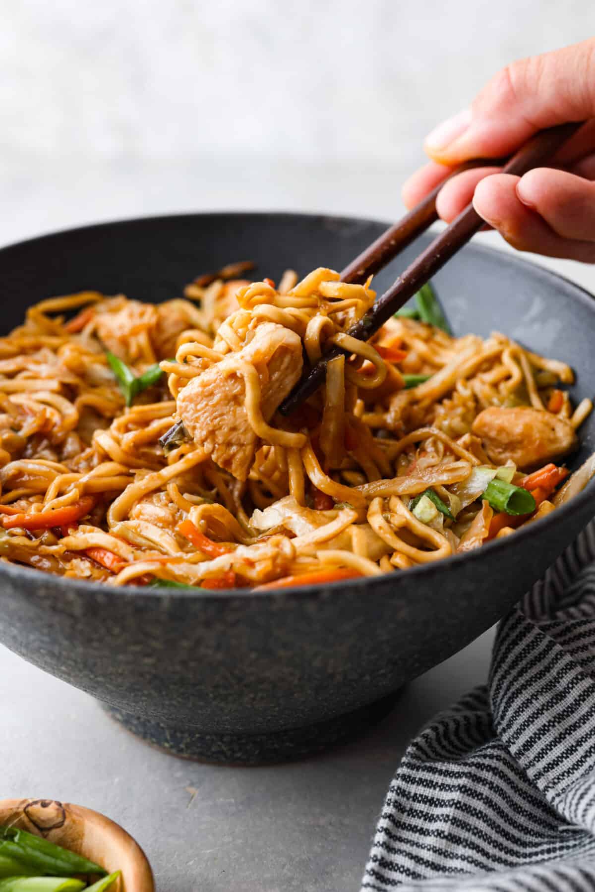 Picking up a bite of noodles and chicken with chopsticks.