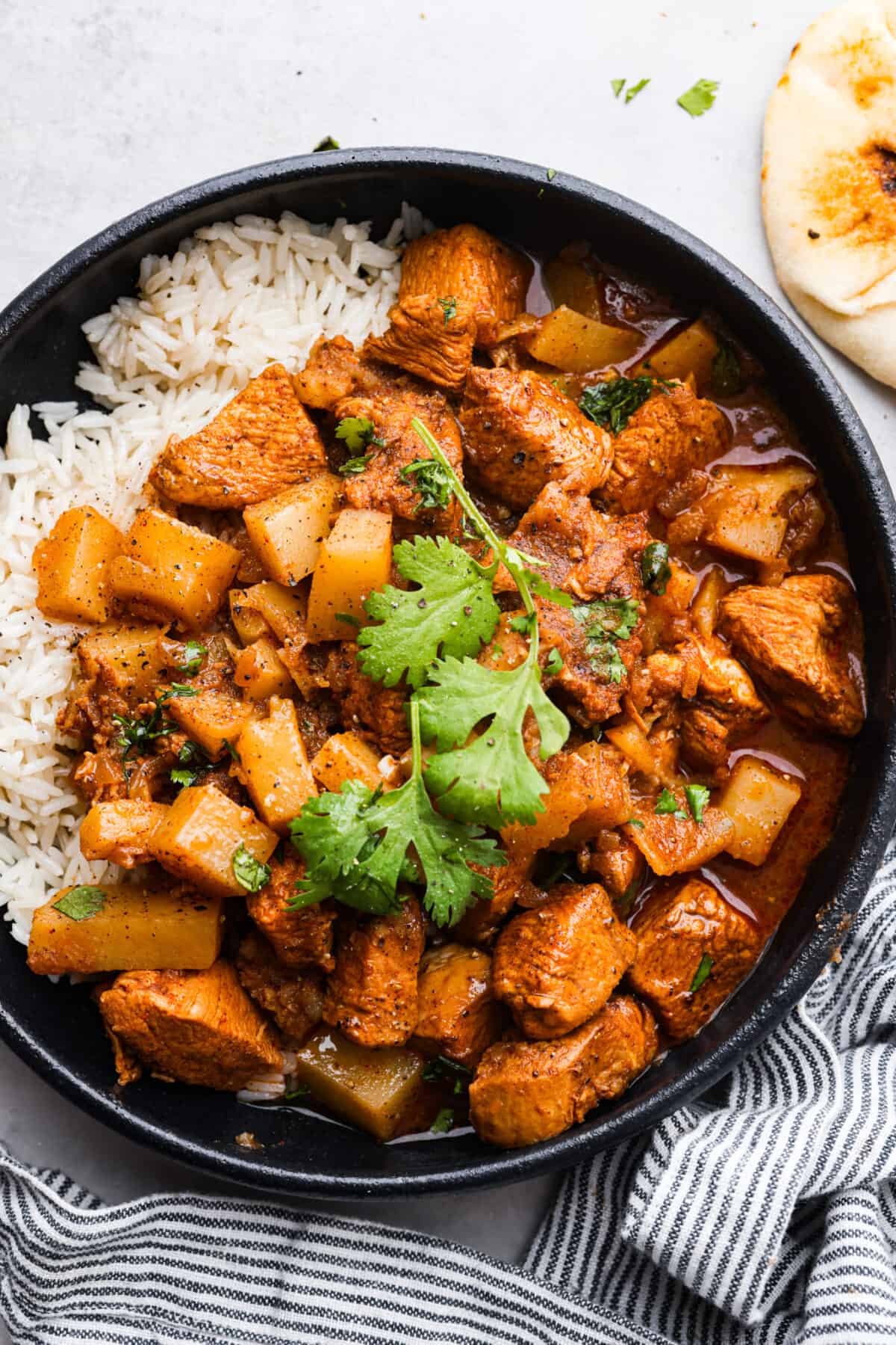 A serving of chicken vindaloo and white rice in a black bowl.