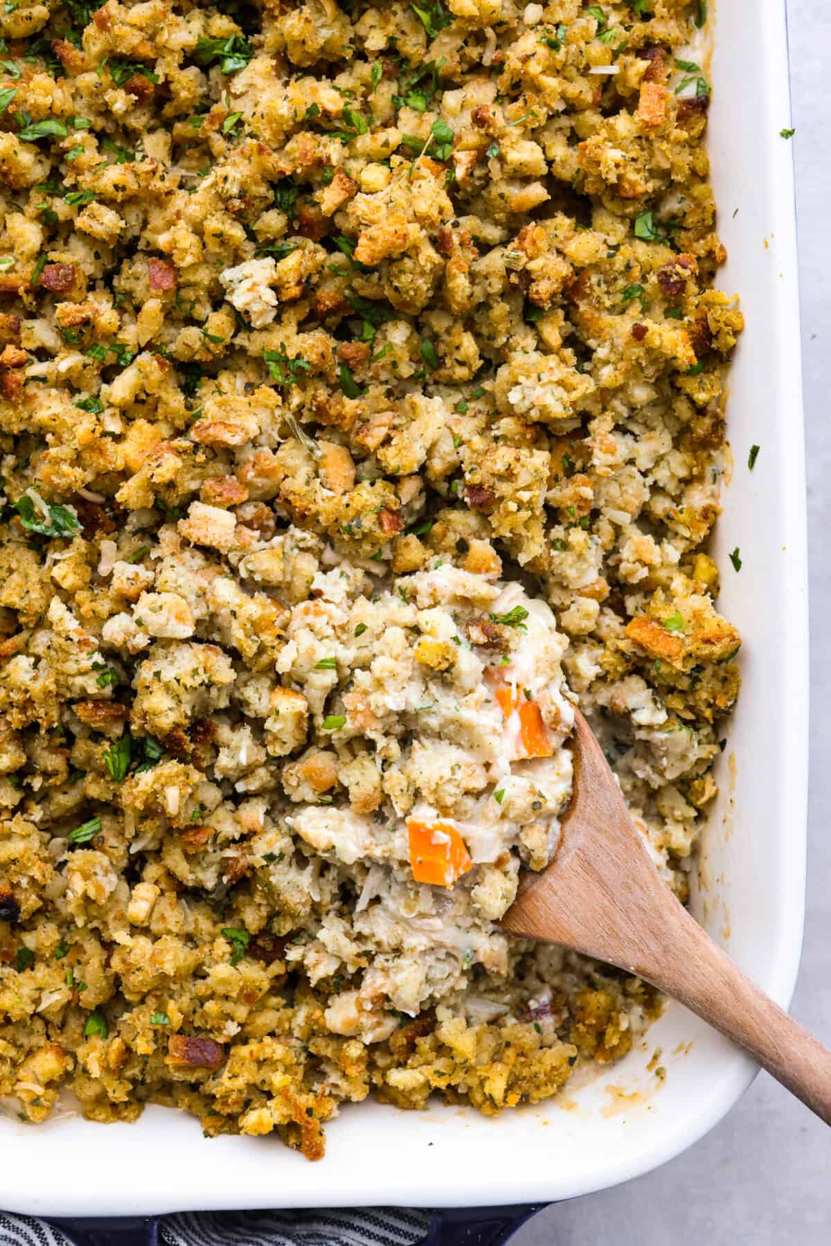 Closeup of a scoop of chicken and stuffing casserole on a wooden spoon.