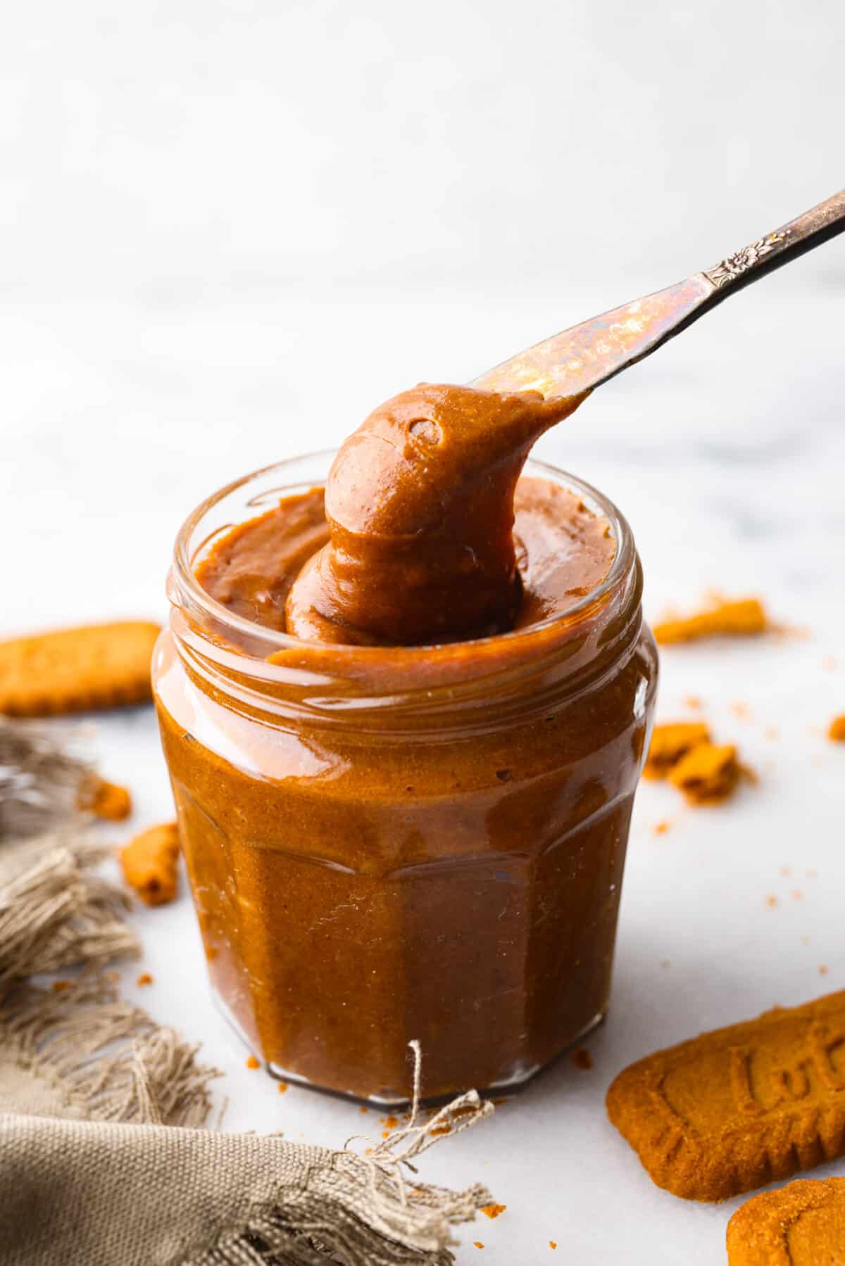 Cookie butter in a jar being scooped out with a silver butter knife. 