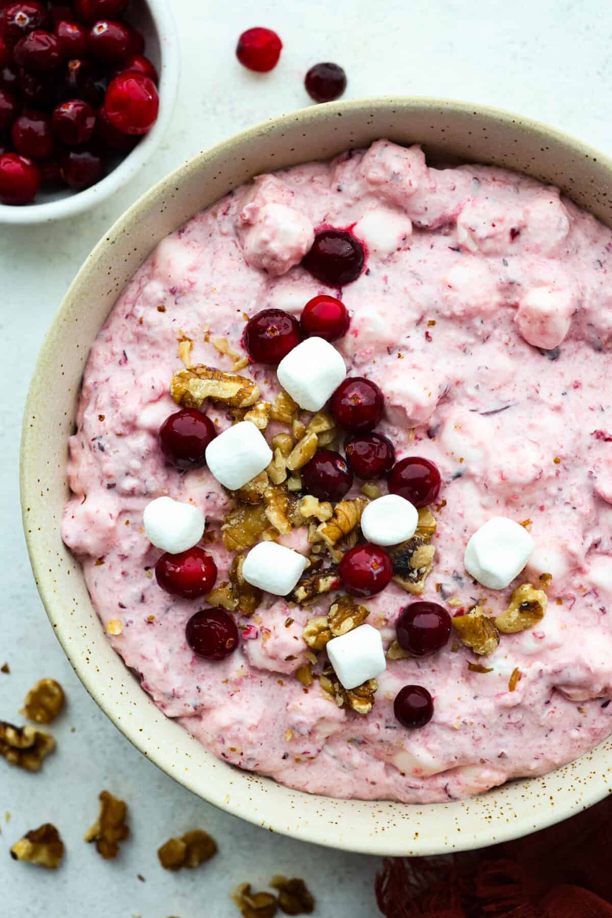 Top-down view of cranberry fluff salad served in a white bowl, topped with marshmallows, cranberries, and chopped walnuts.