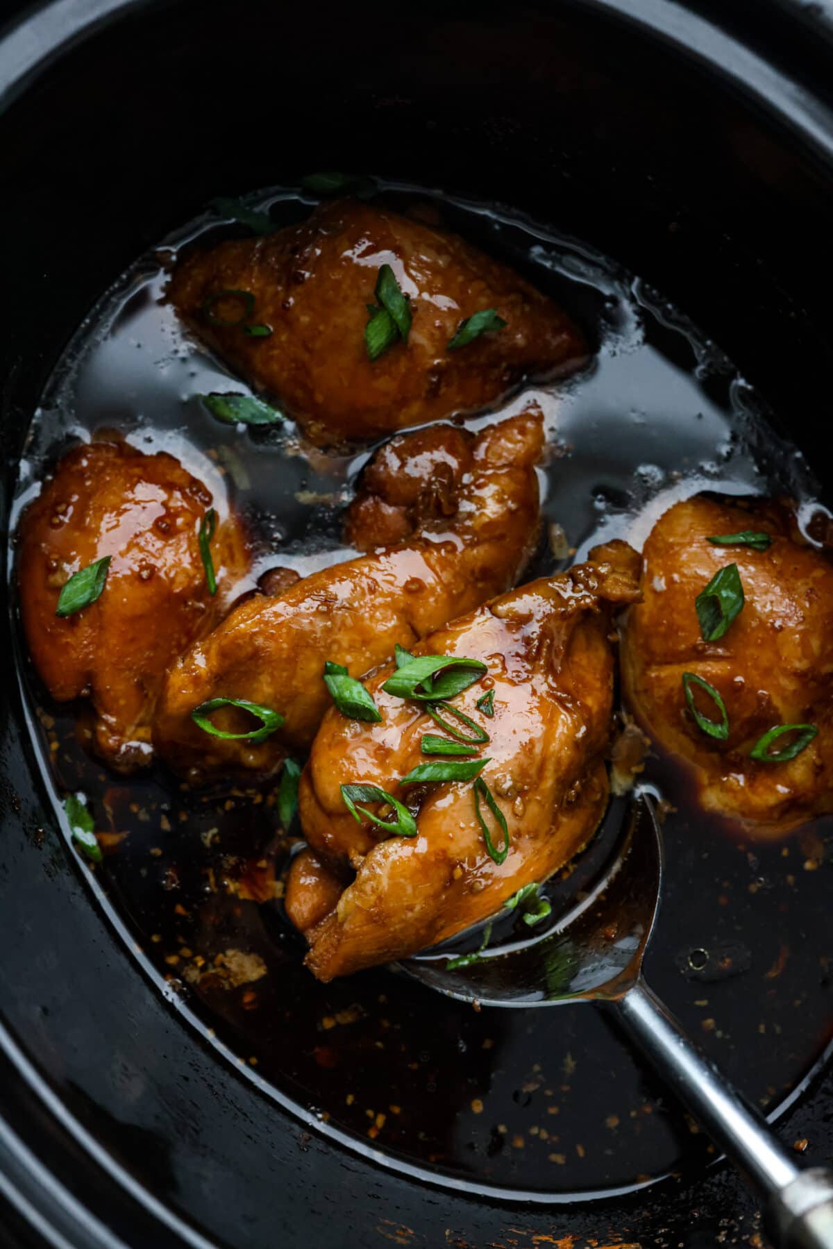 Top view of crockpot bourbon chicken in a crockpot before it is shredded. Garnished with sliced green onion.