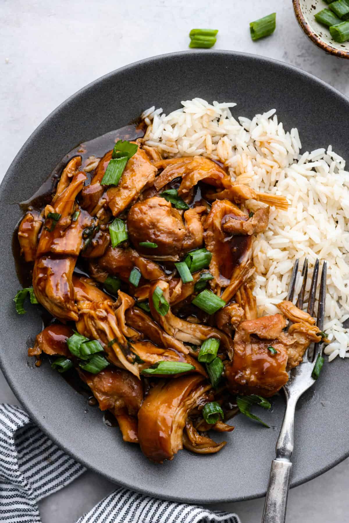 Close top view of shredded crockpot bourbon chicken on a gray plate with rice.