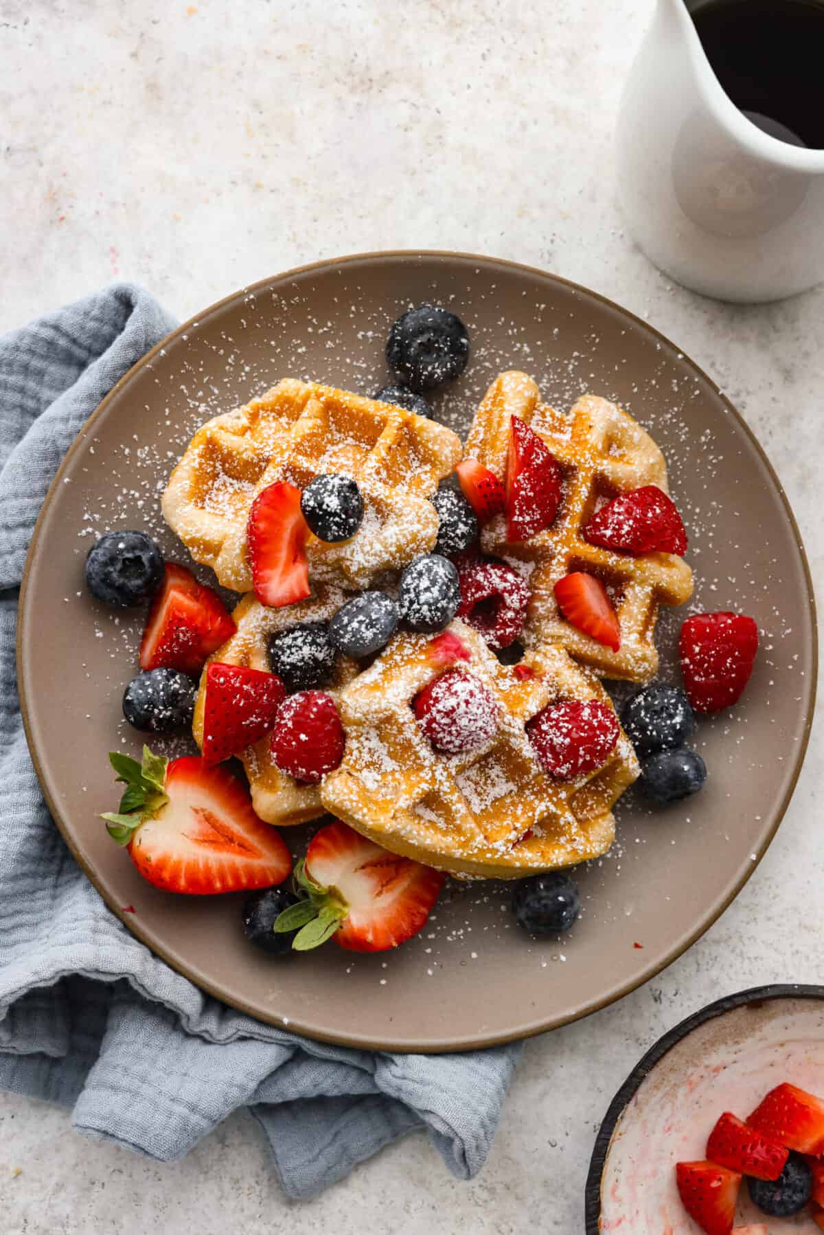 3 croffles served with powdered sugar and fruit on a gray plate.