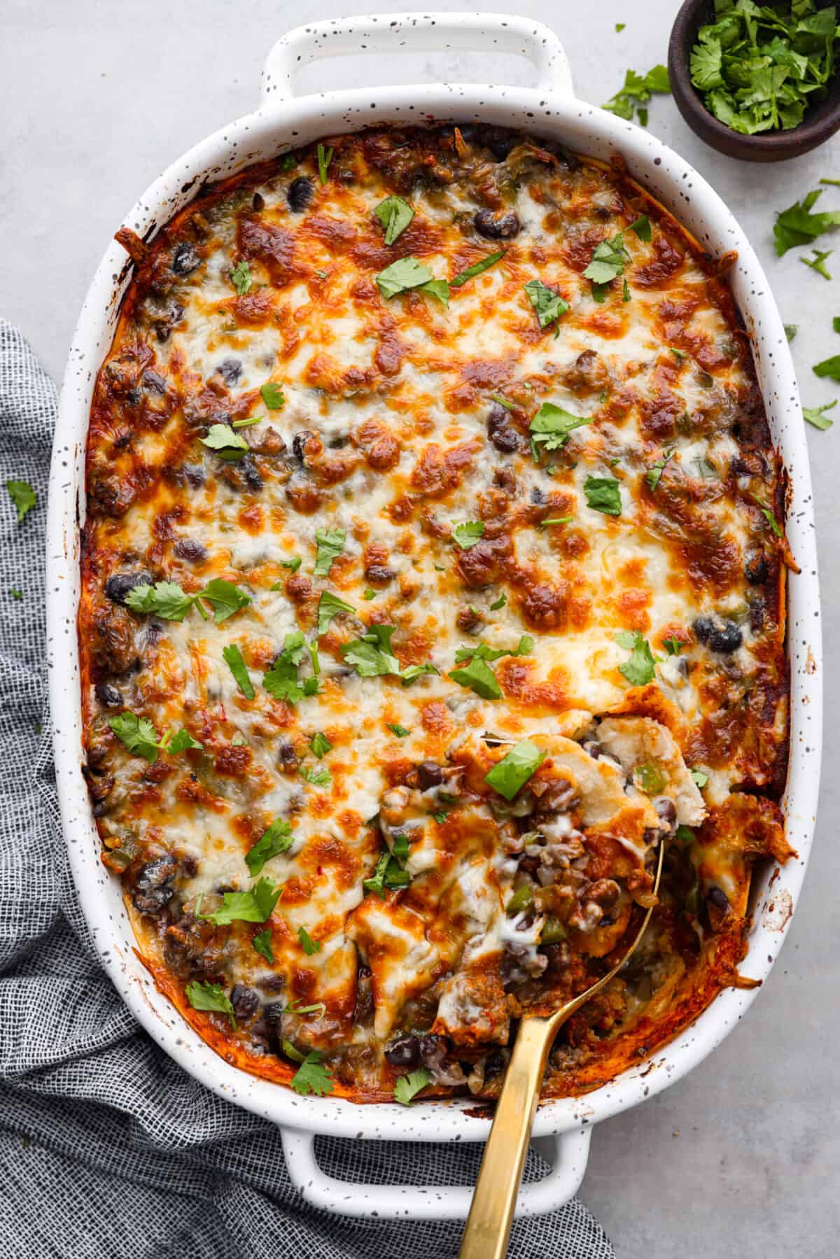 Top-down view of a baked enchilada pie. There is a golden metal spoon scooping into it.