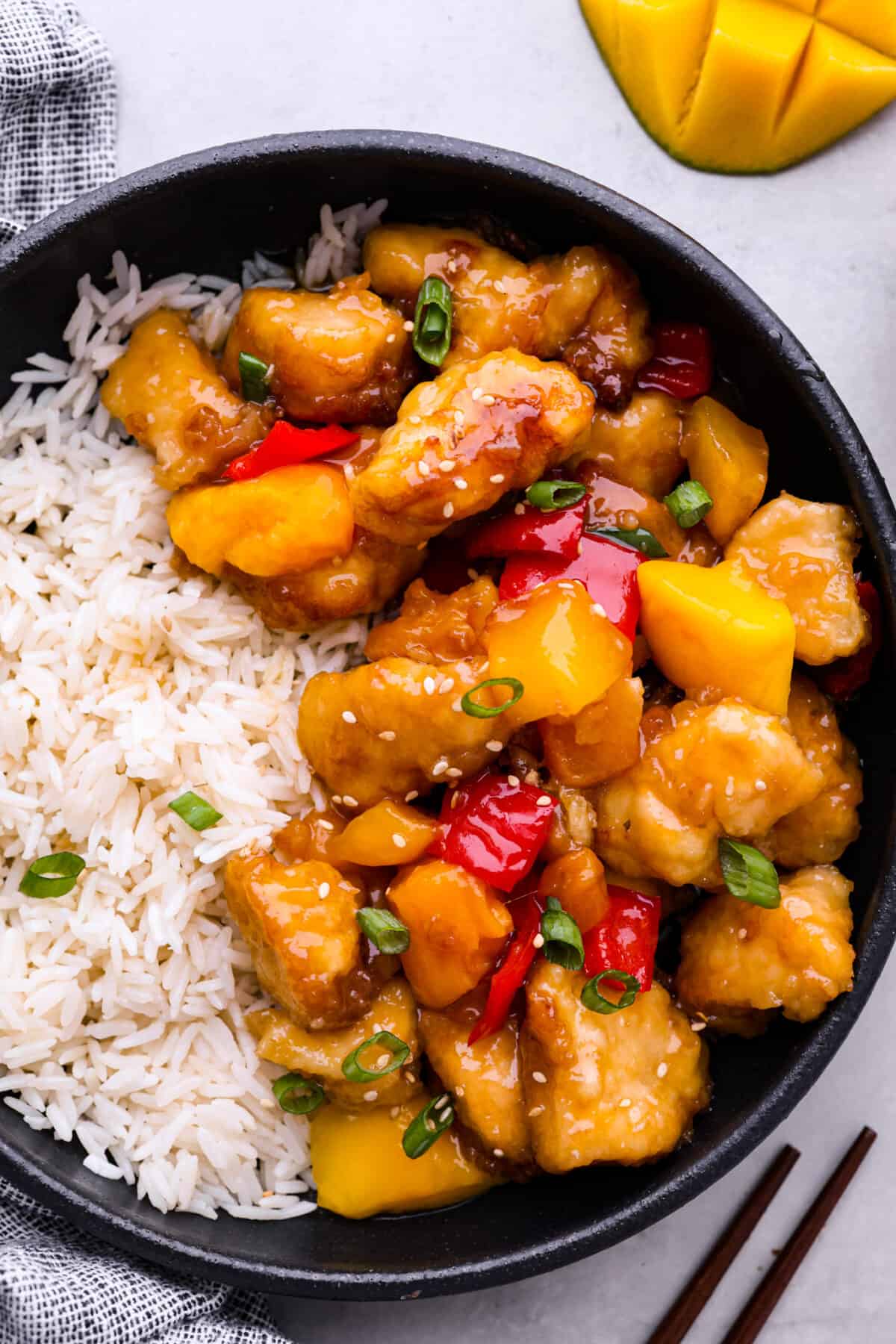 Mango chicken served with white rice in a black bowl.