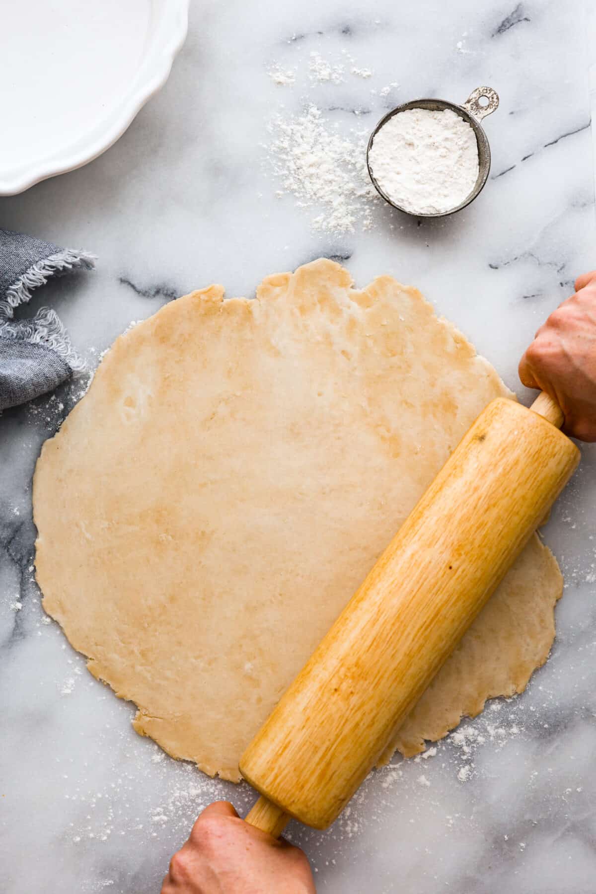 Pie dough being rolled out with a wooden roller. 