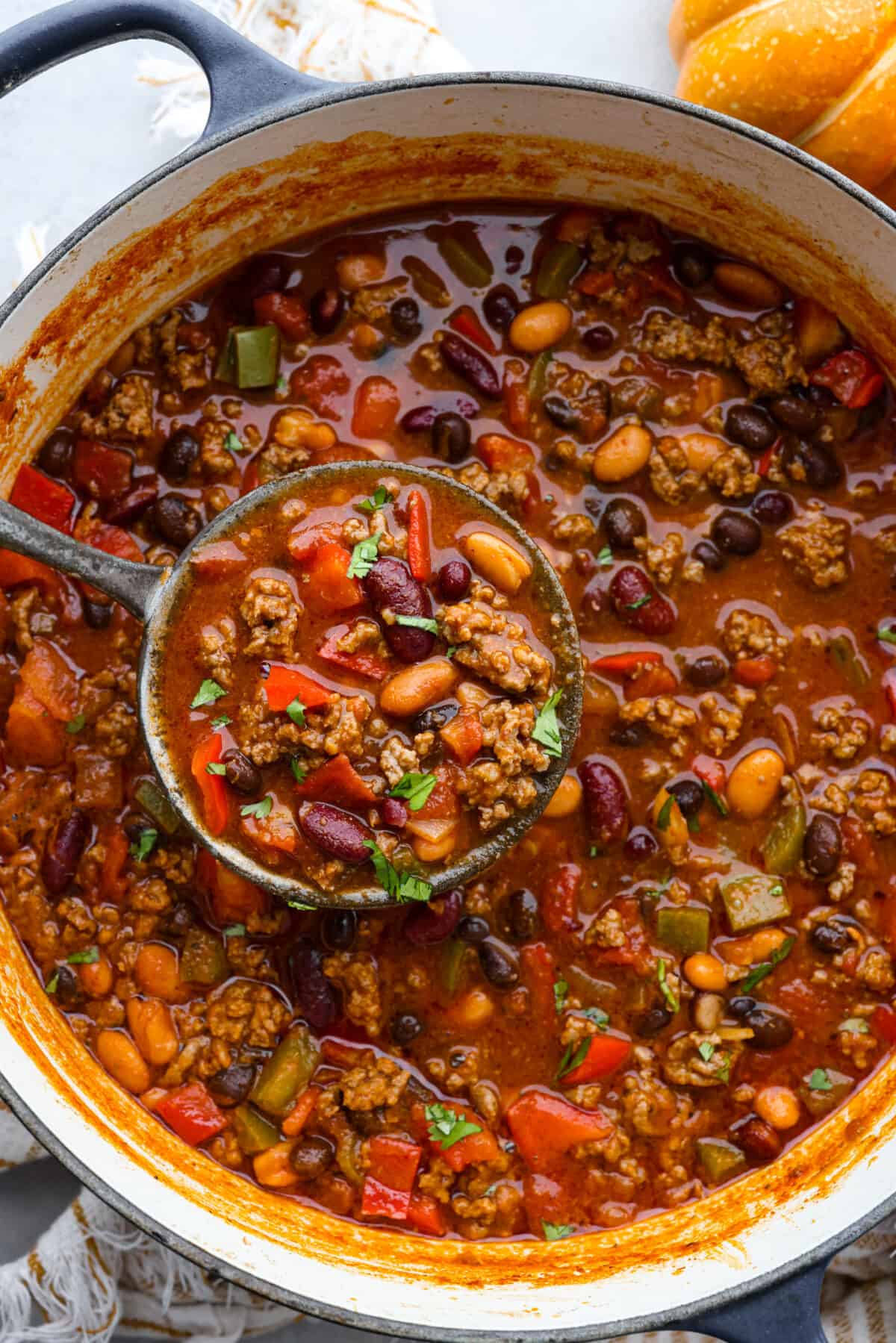 Pumpkin chili in a large blue and white pot, being scooped up with a ladle.