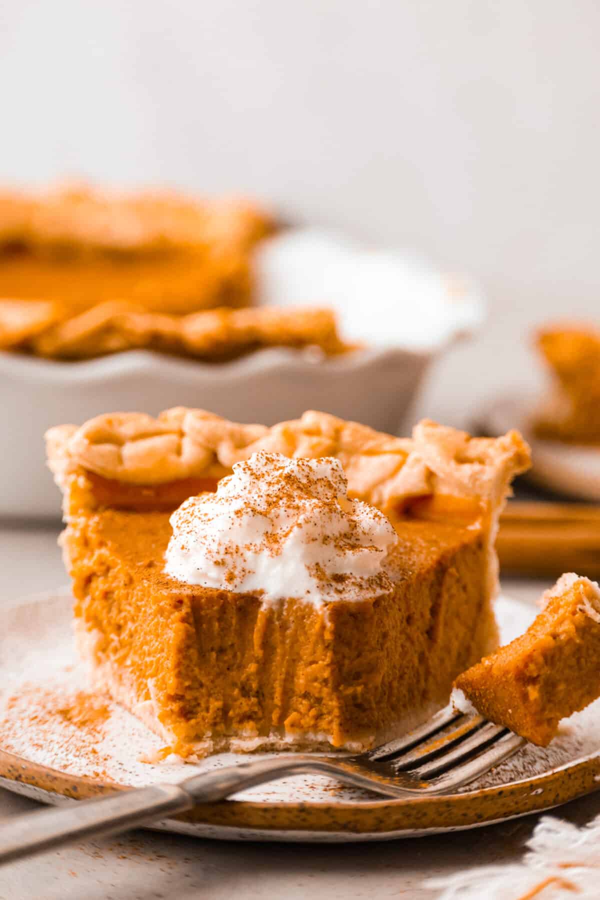 Front view of a slice of pumpkin pie with a bite taken out of it.