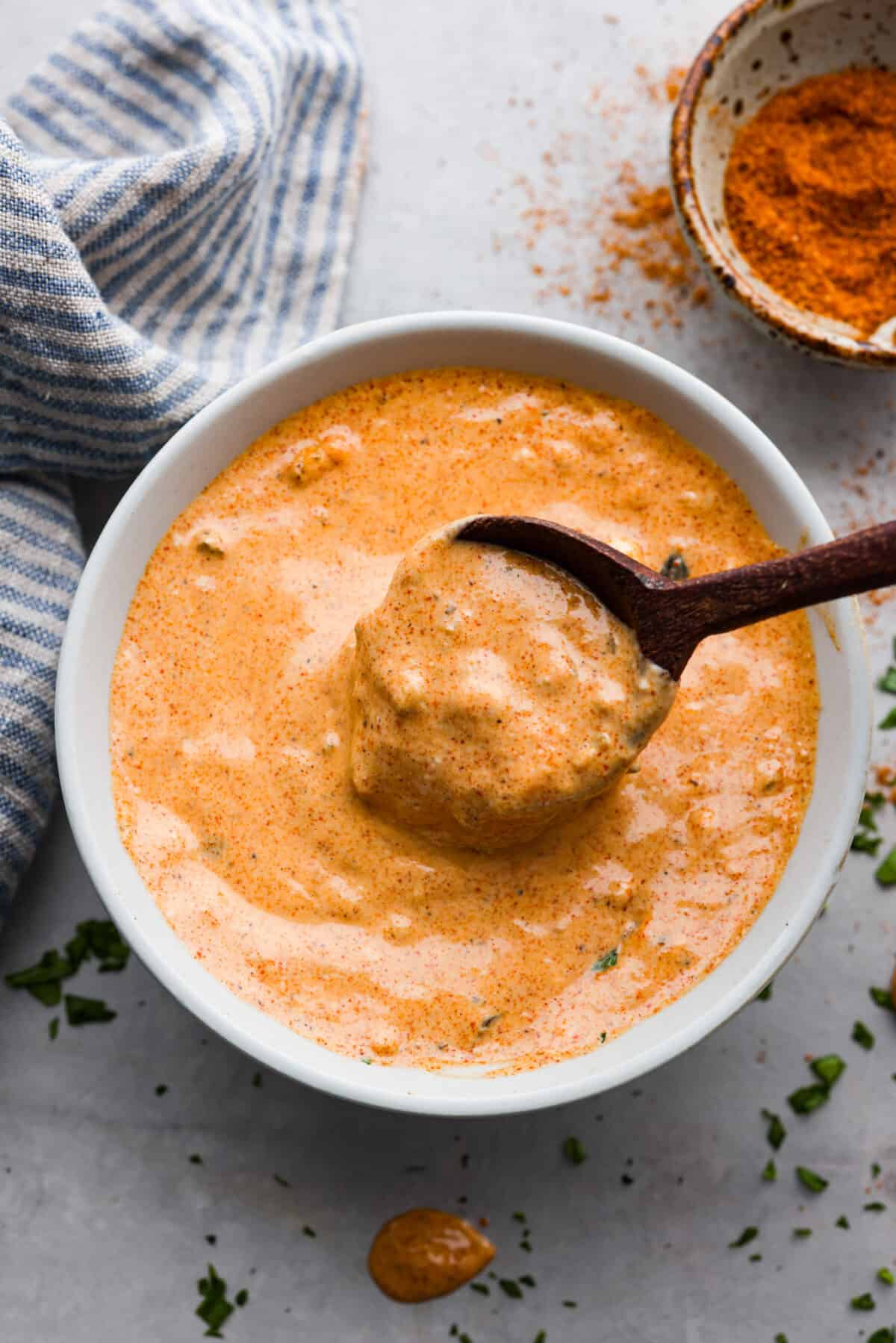 Remoulade sauce in a white bowl, being mixed with a wooden bowl.