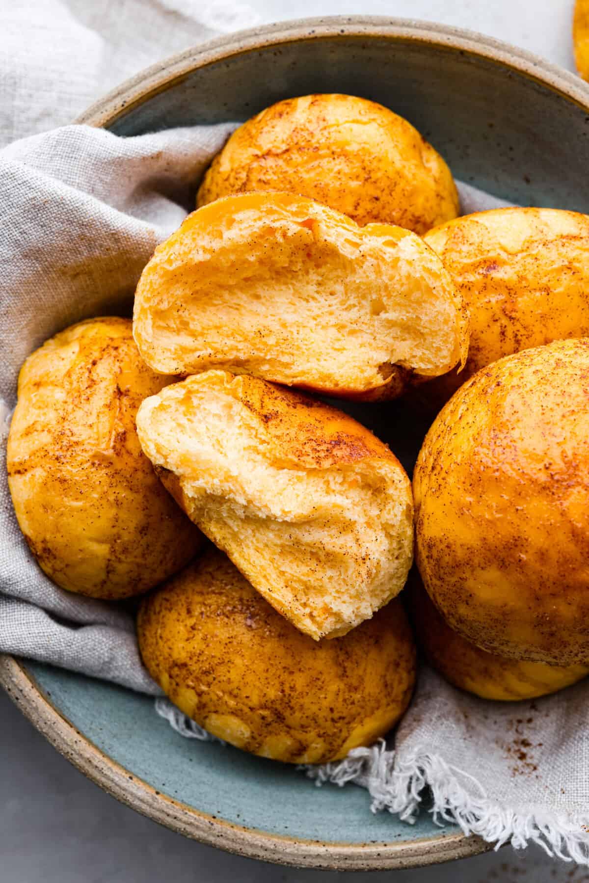 Close view of a bowl of sweet potato rolls with the roll on top broken in half.