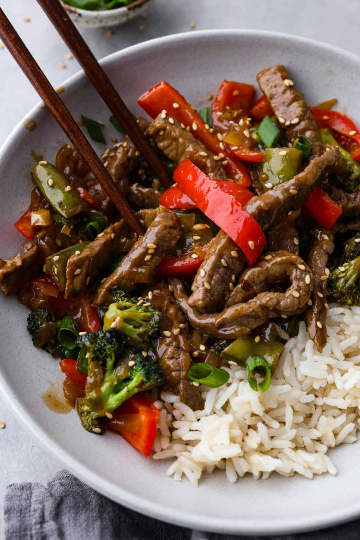 A bowl of szechuan beef served with chopsticks.