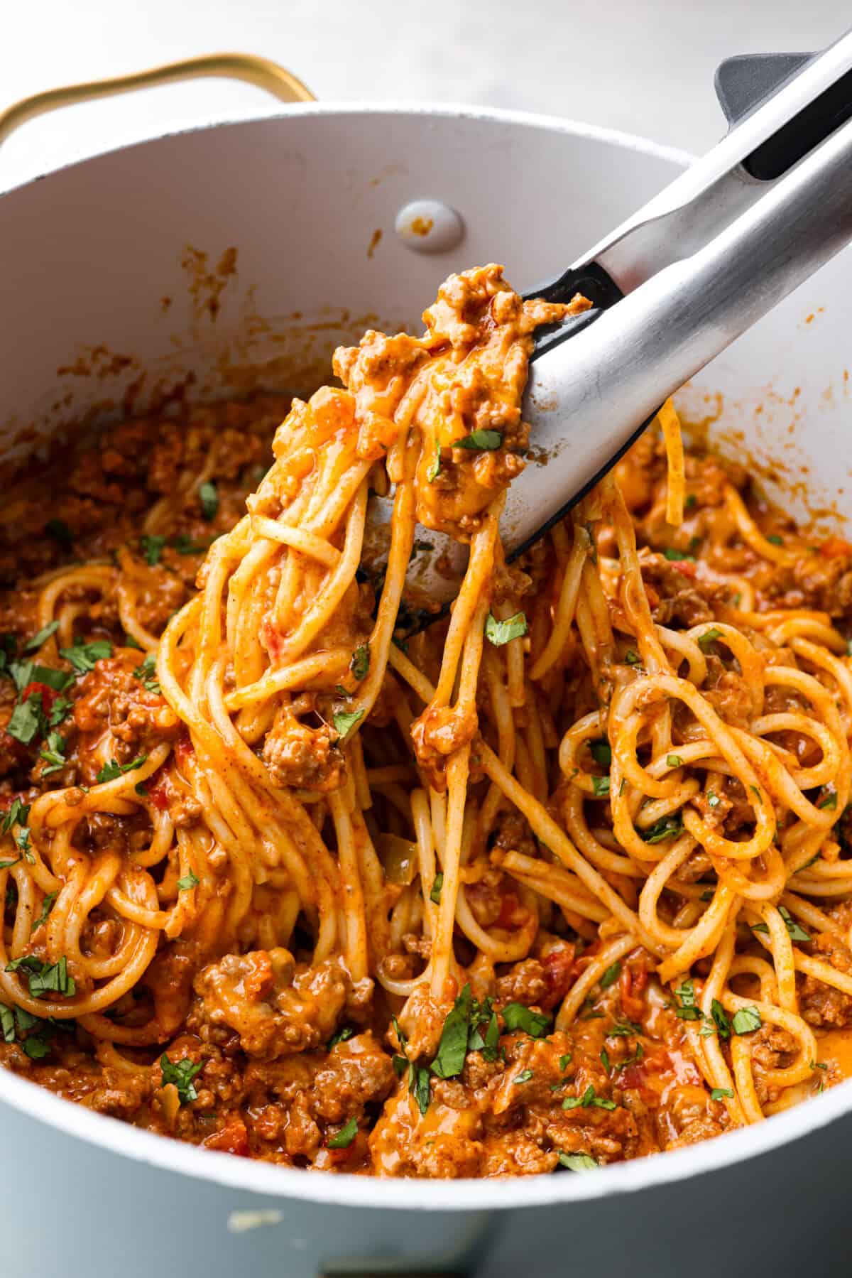 Taco spaghetti in a large pot, being picked up with tongs.