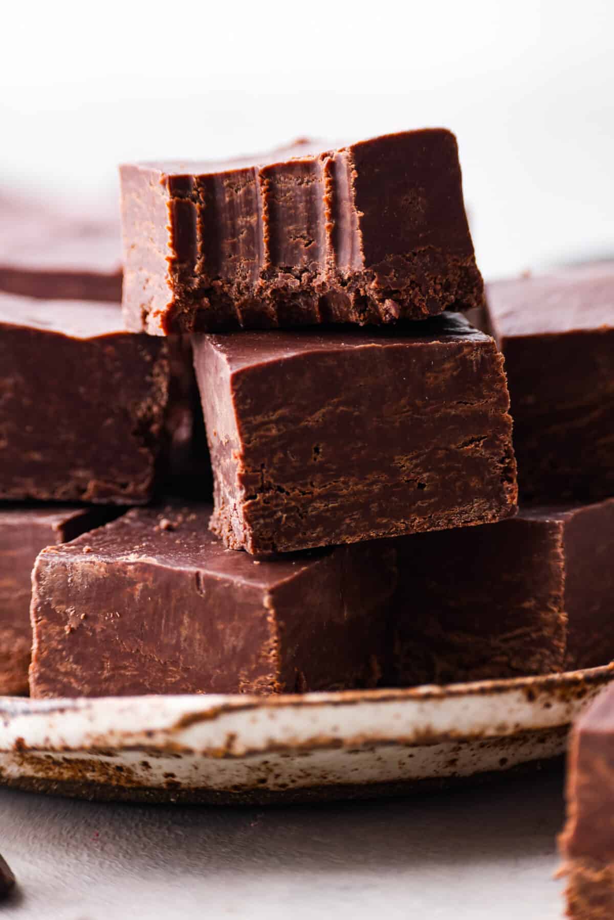 Close view of 2 ingredient fudge squares stacked on a plate. The top piece of fudge has a bite out of it.