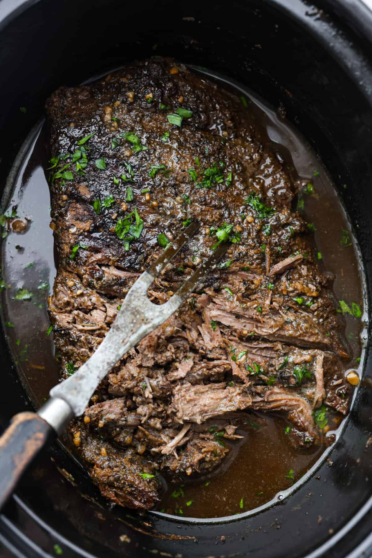 Balsamic beef being shredded in the bottom of a slow cooker.