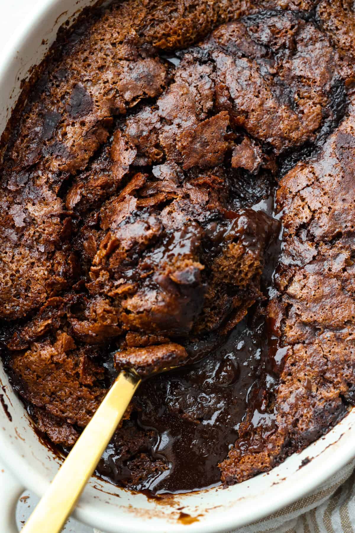 a close up of chocolate cobbler in a pan with a large, gold serving spoon. 