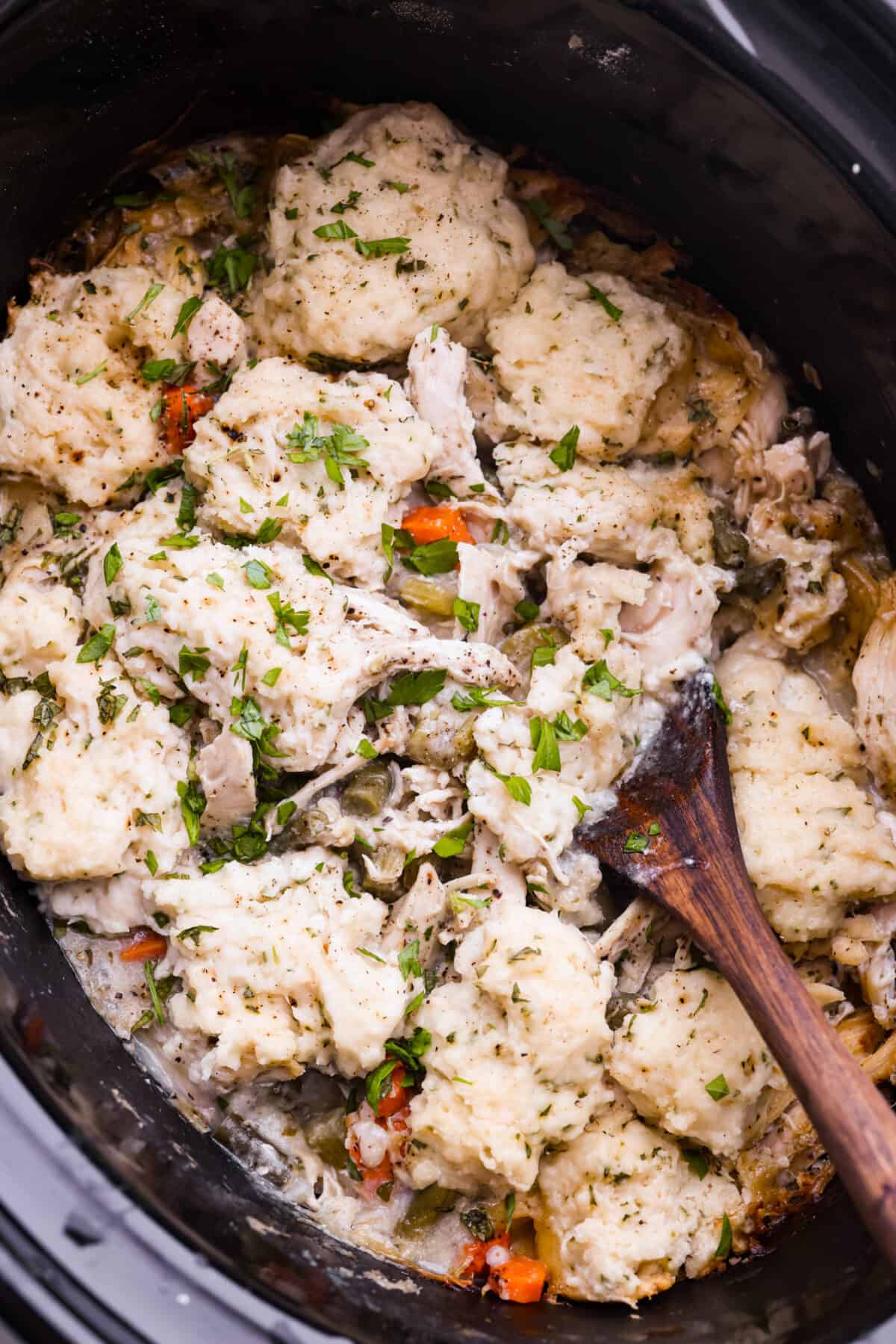 Top view of crockpot chicken and dumplings in a crockpot with a wooden spoon.