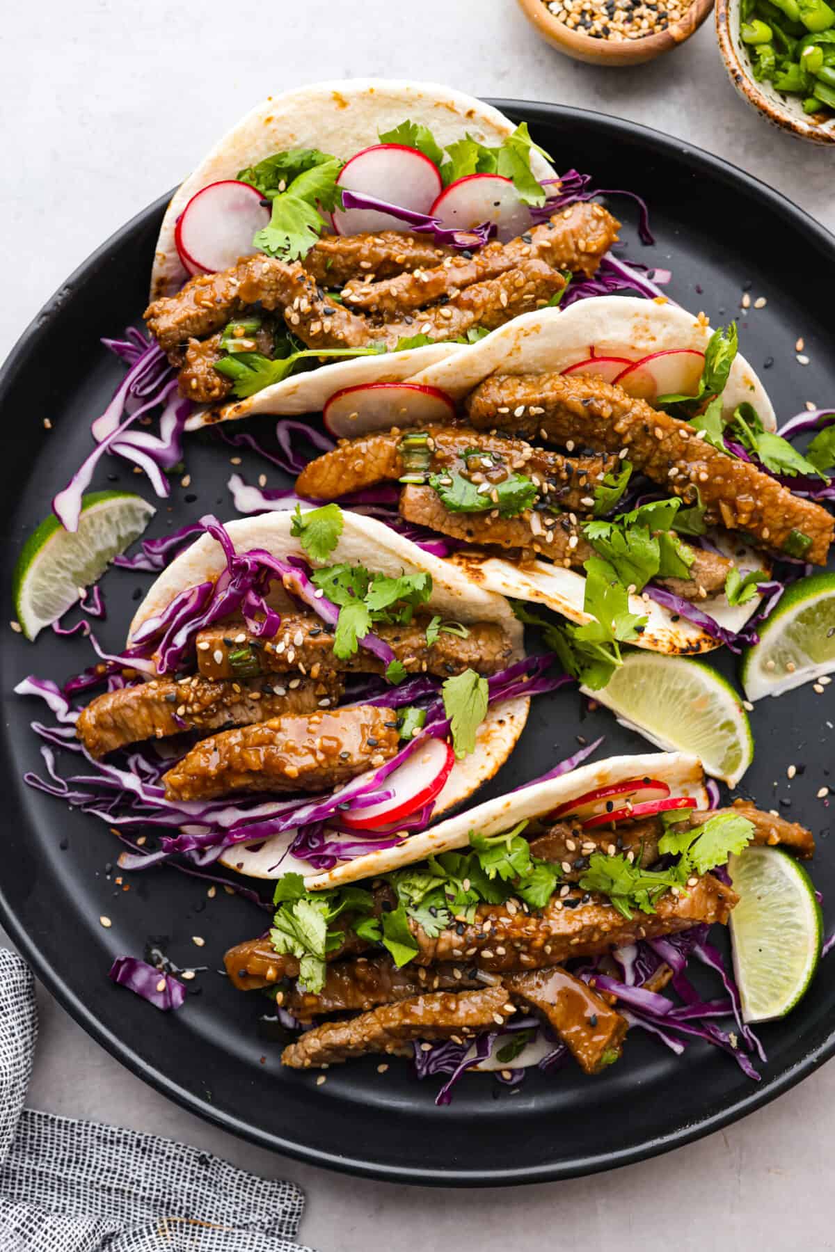 Top view of Korean tacos on a black plate garnished with toppings and limes.