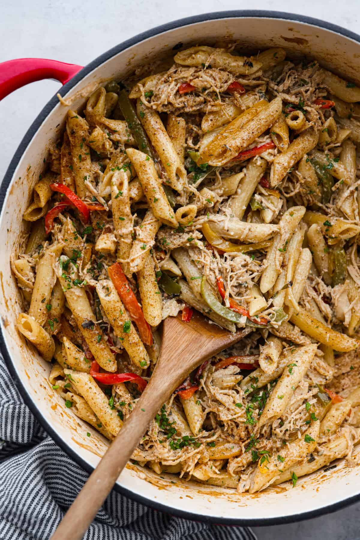 Rasta pasta in a blue and white skillet, being mixed with a wooden spoon.