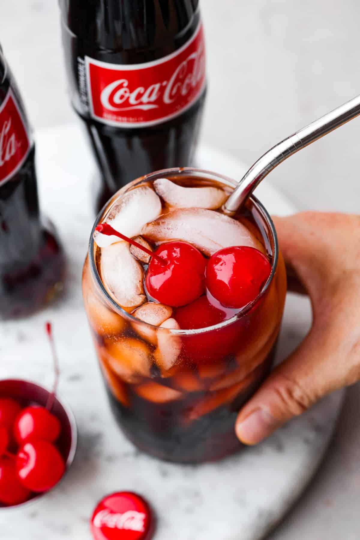 Top view of a hand holding a drink with a straw and cherries on top.