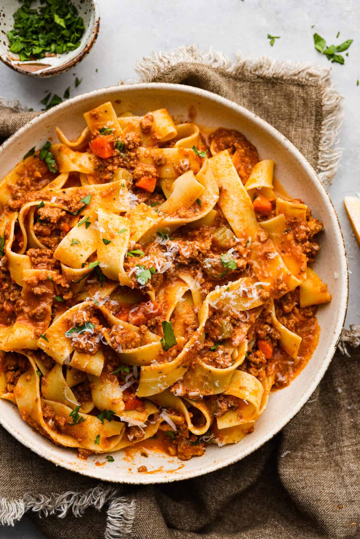 A bowl of ragu with pasta. Topped with fresh parsley and freshly grated cheese. 