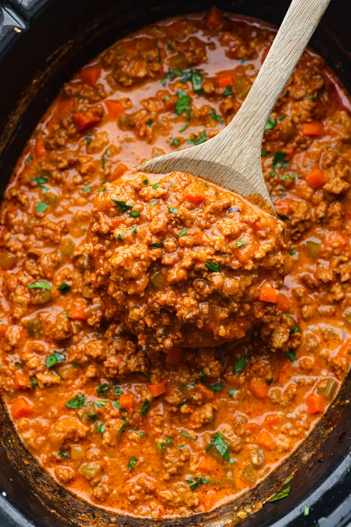 Finished ragu sauce in the slow cooker with a wooden spoon scooping some out. 