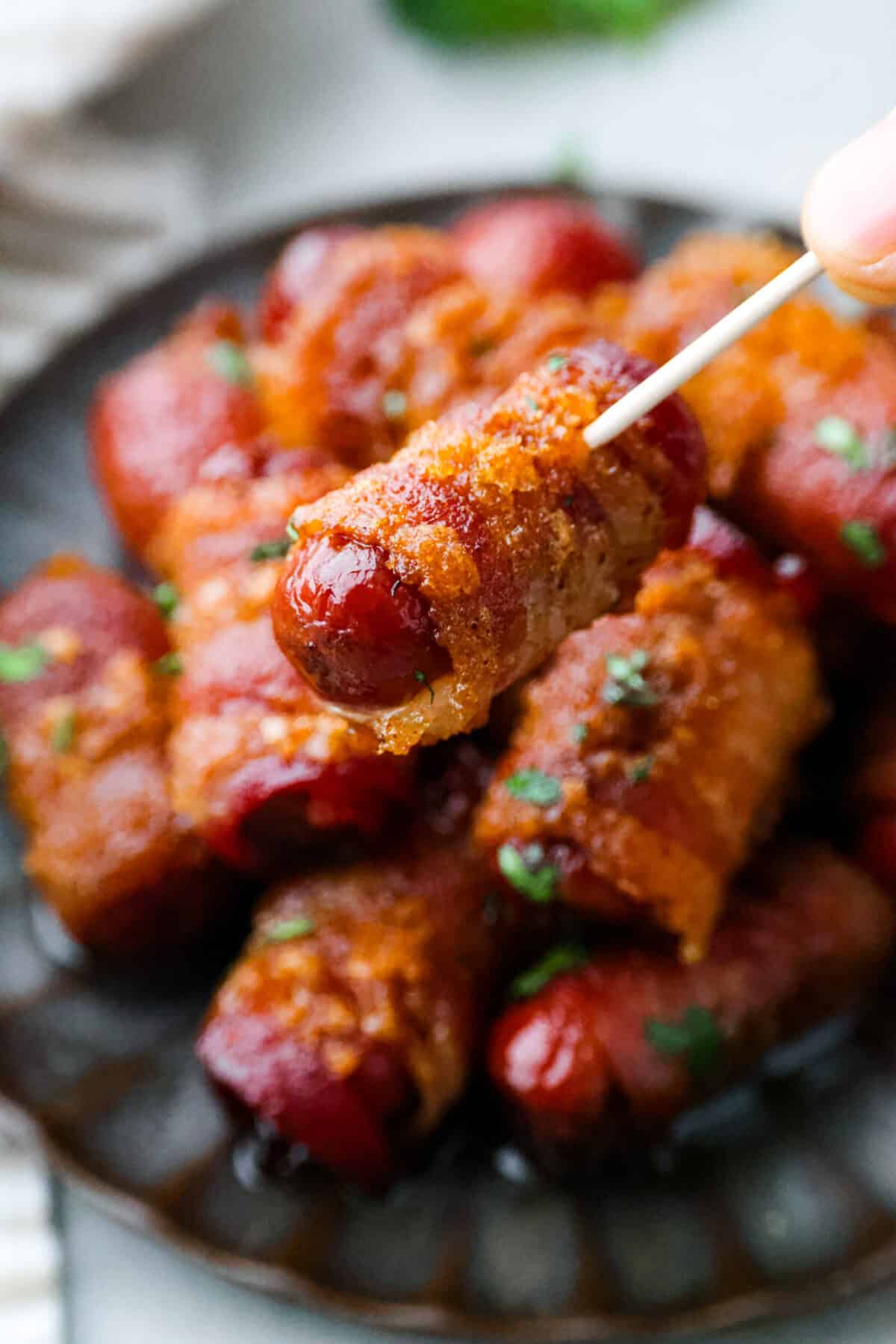 Close view of a toothpick holding a bacon wrapped smokie.