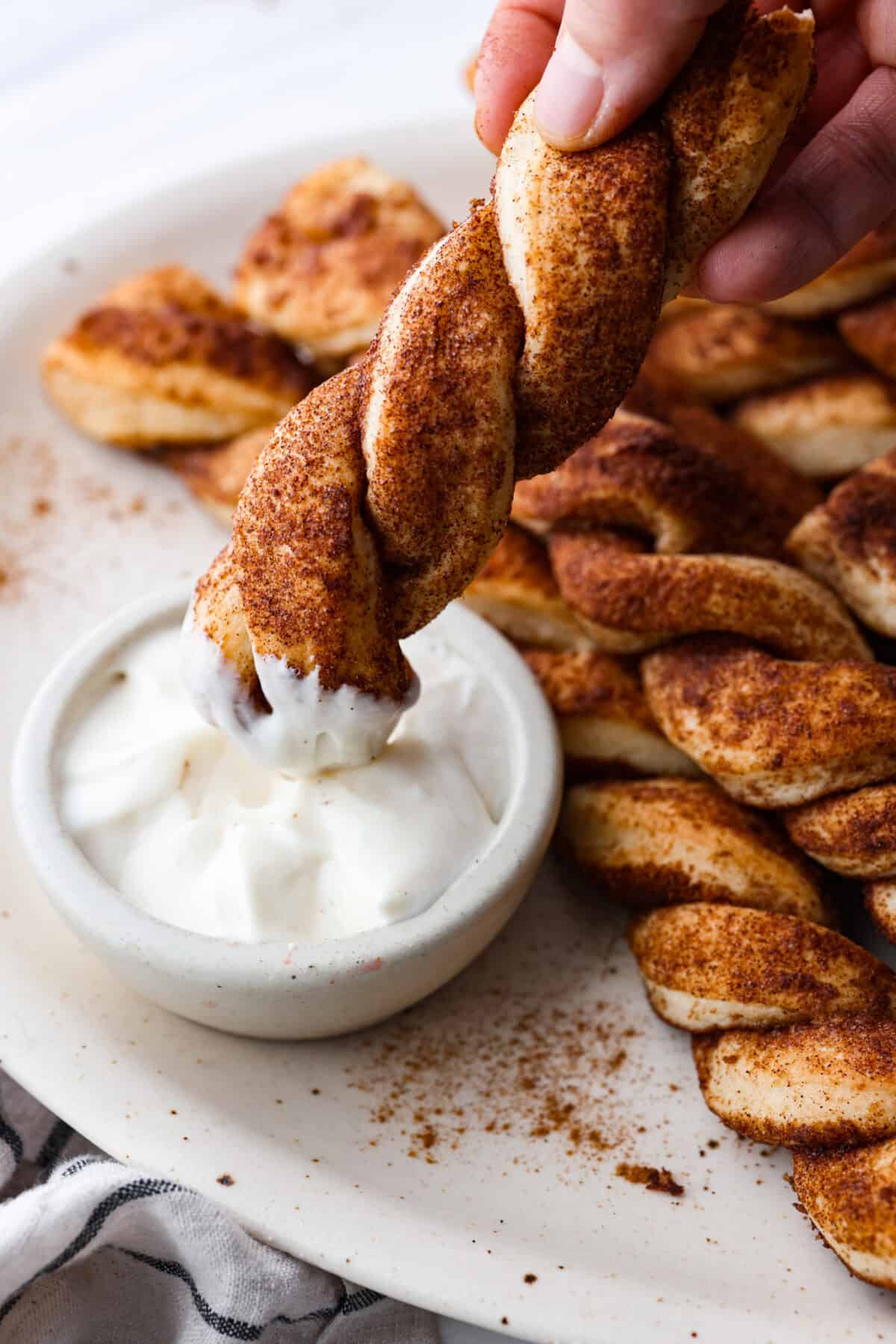 Close view of a cinnamon bread twist dipping in frosting.