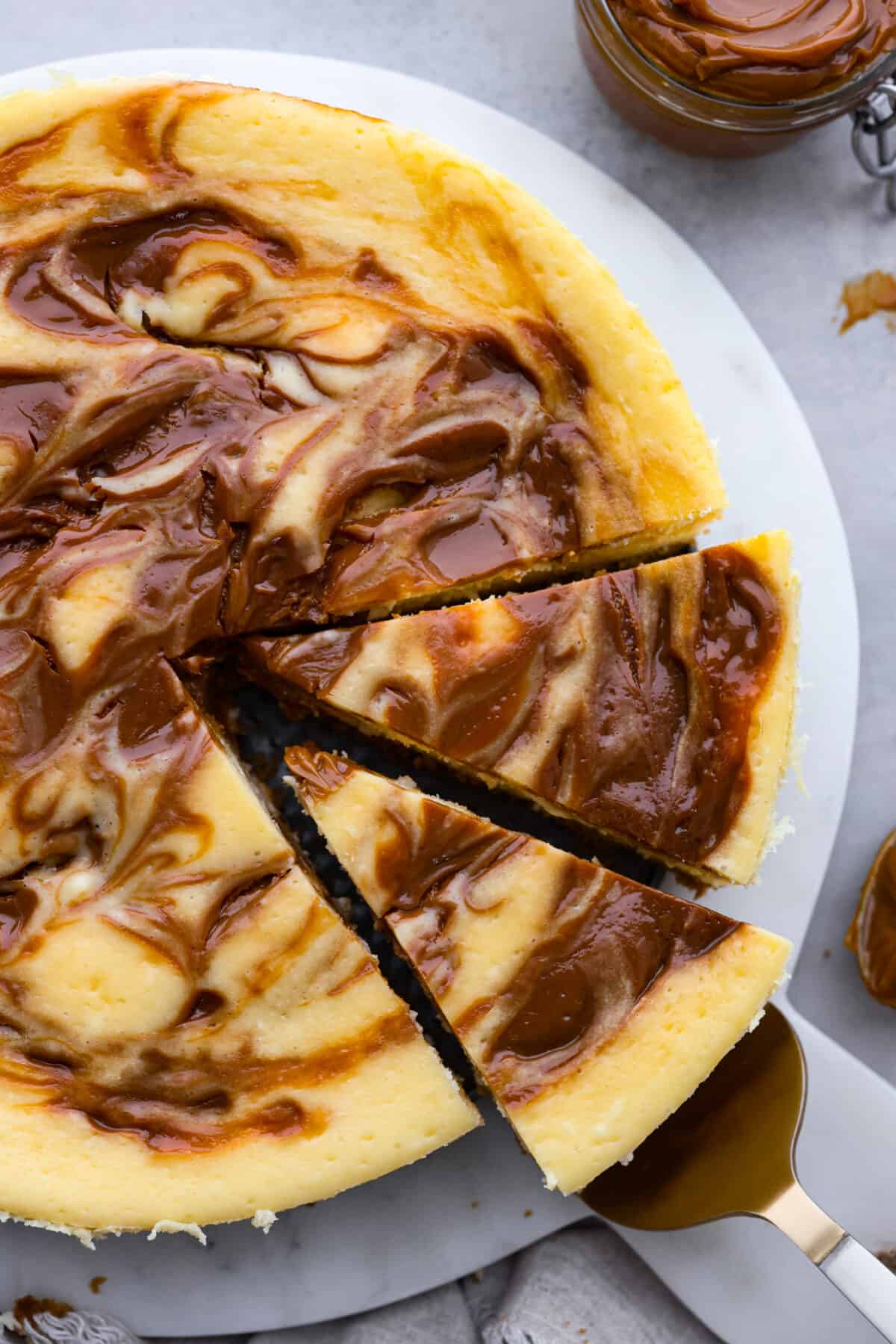 Top-down view of dulce de leche cheesecake, cut into slices and being served with a metal cake spatula.