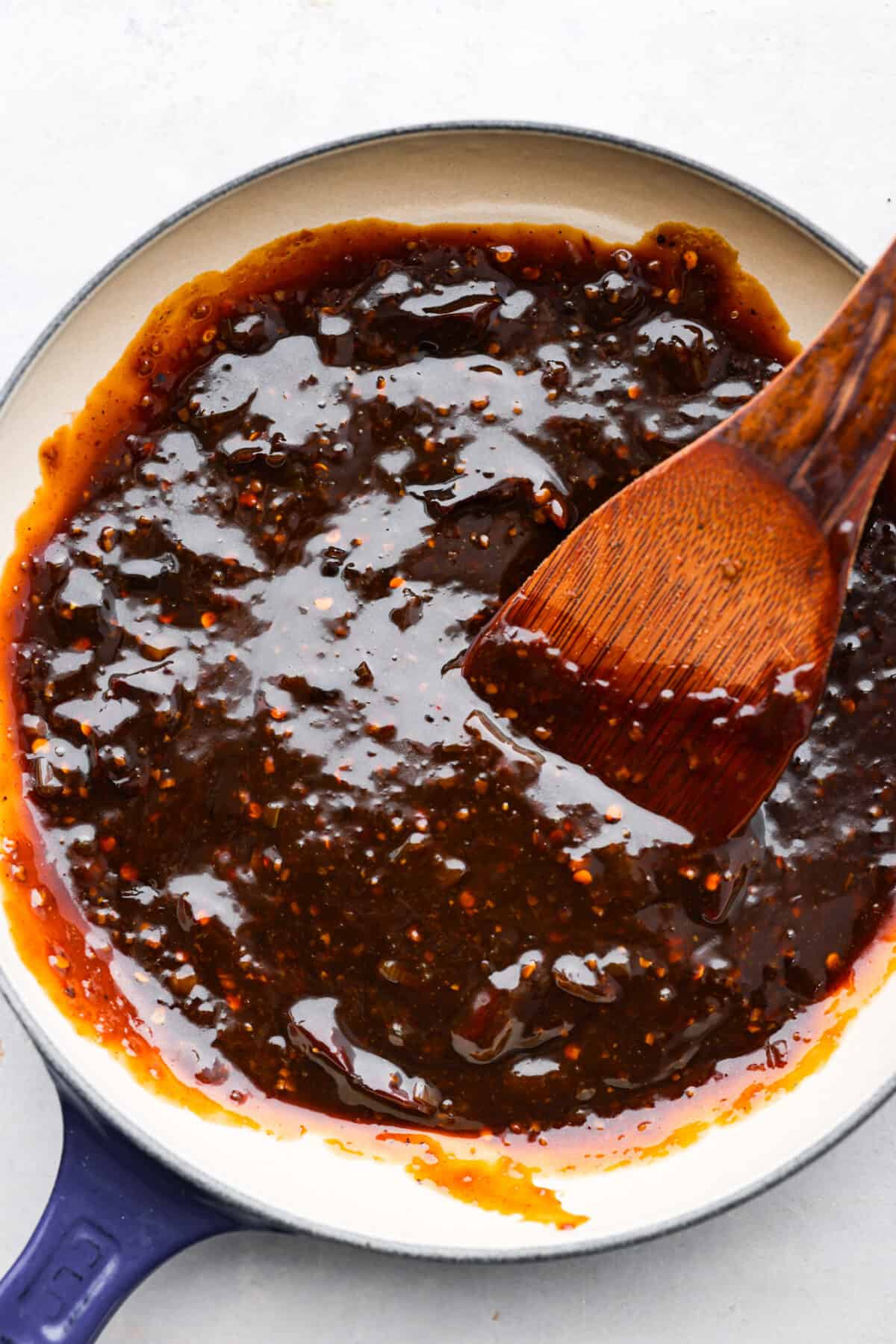 Kung pao sauce being mixed with a wooden spoon in a blue and white skillet.