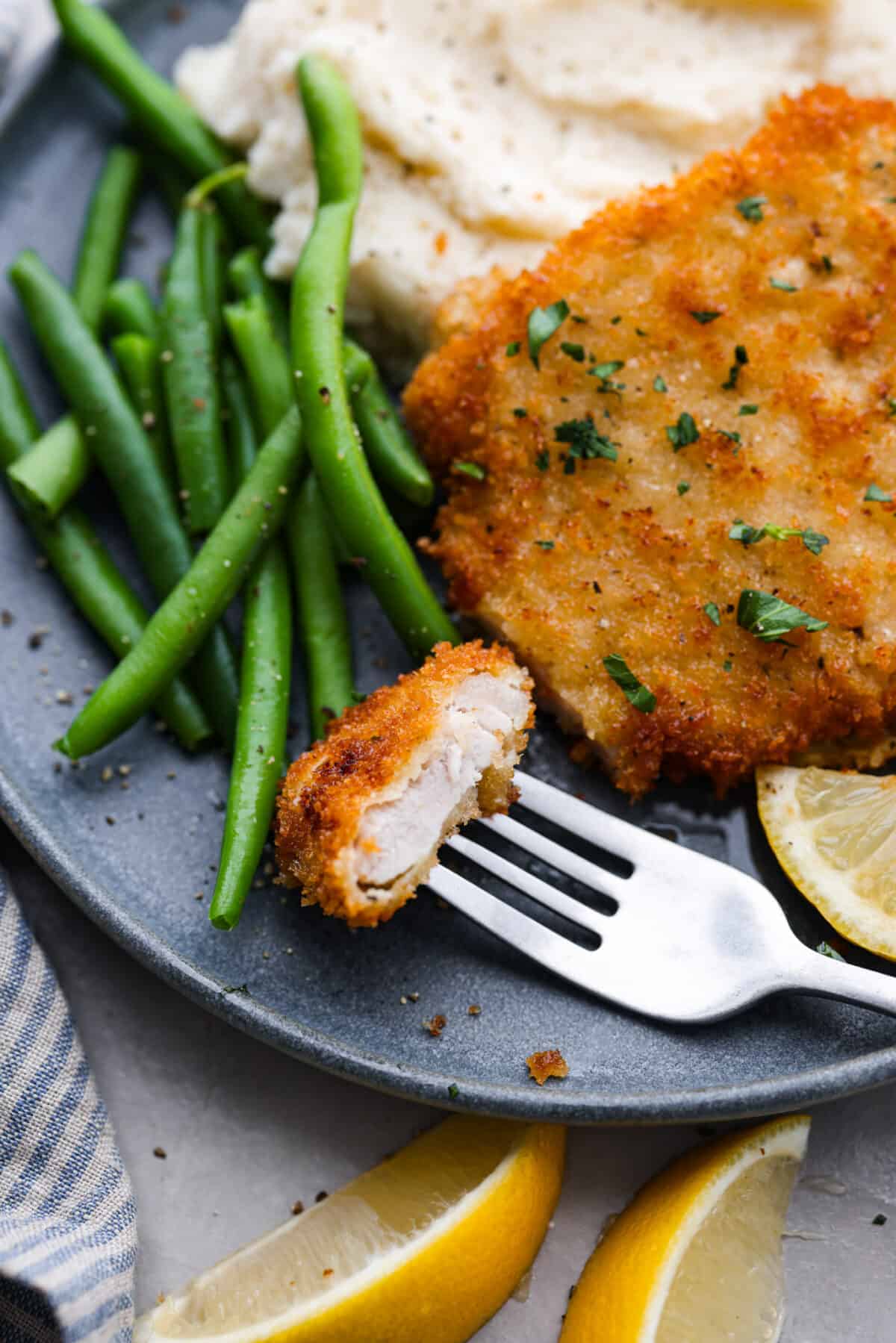 Closeup of a bite of pork cutlet, served with green beans.