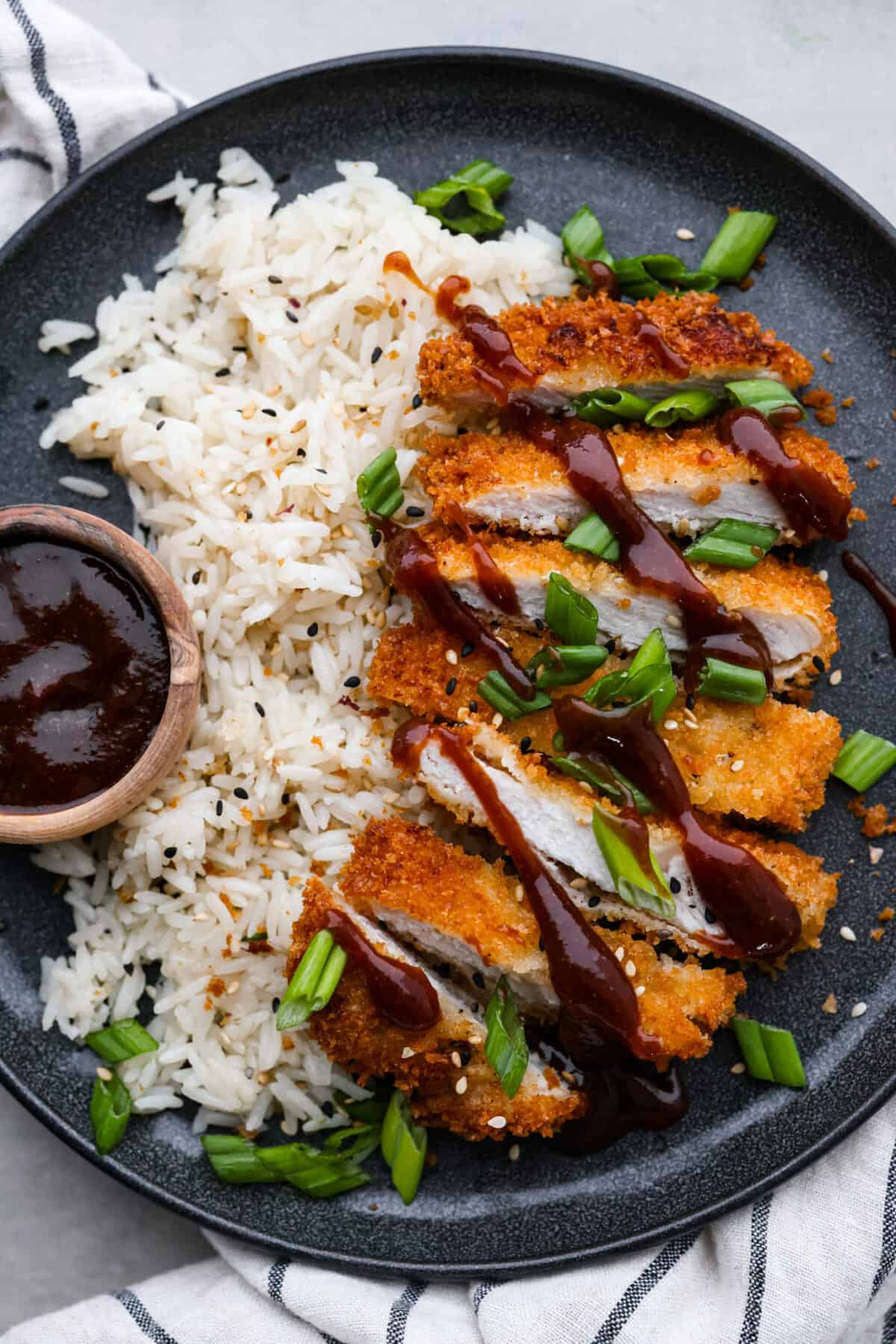 Sliced pork katsu served with rice on a black plate.