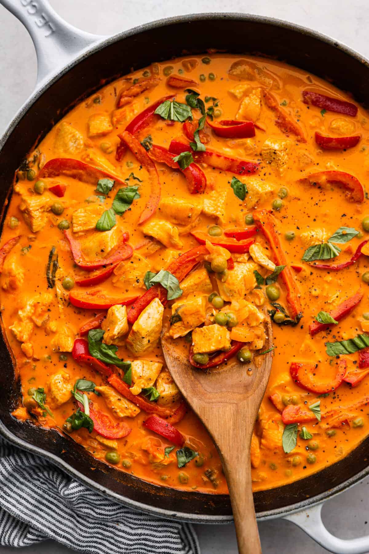 Top-down view of red curry in a skillet, being stirred with a wooden spoon.