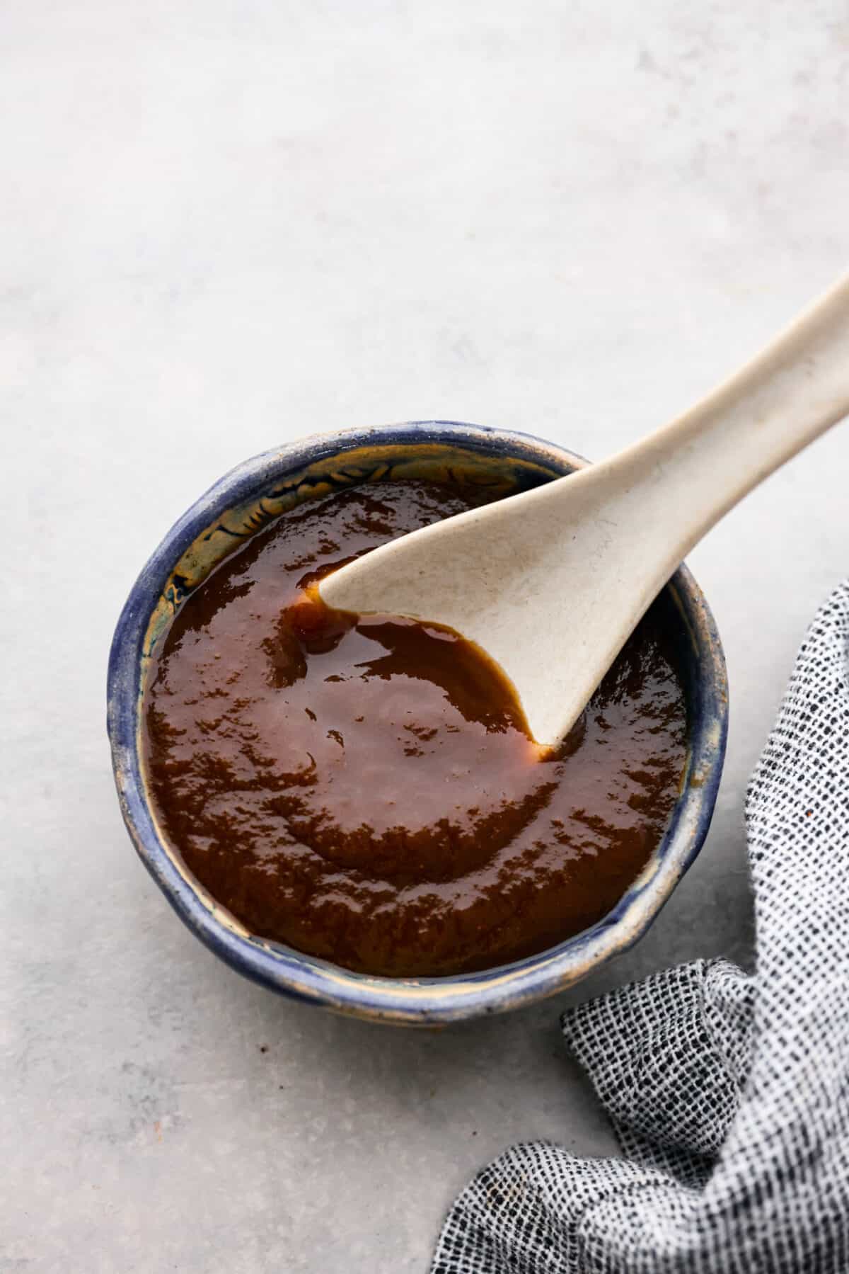 Top view of tamarind suce in a blue bowl. A soup spoon is lifting sauce up from the bowl.