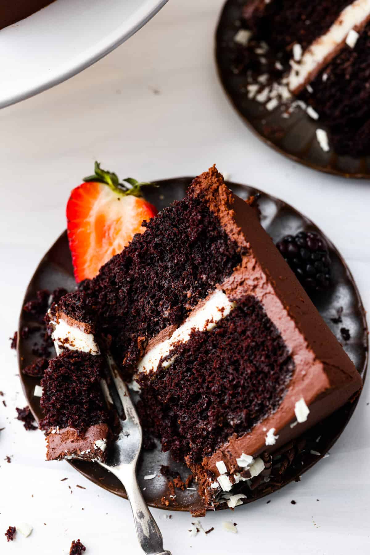 A slice of chocolate cake on a black plate with a bite taken out of it.