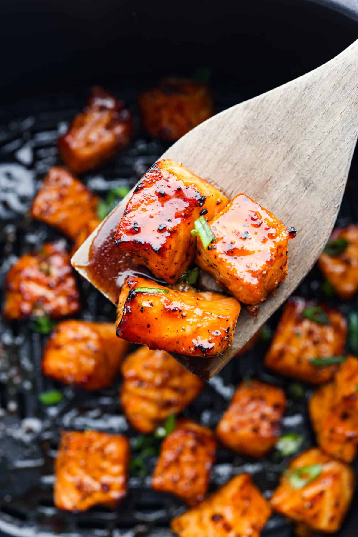 Close view of a wood spatula lifting up salmon bites in the air fryer.