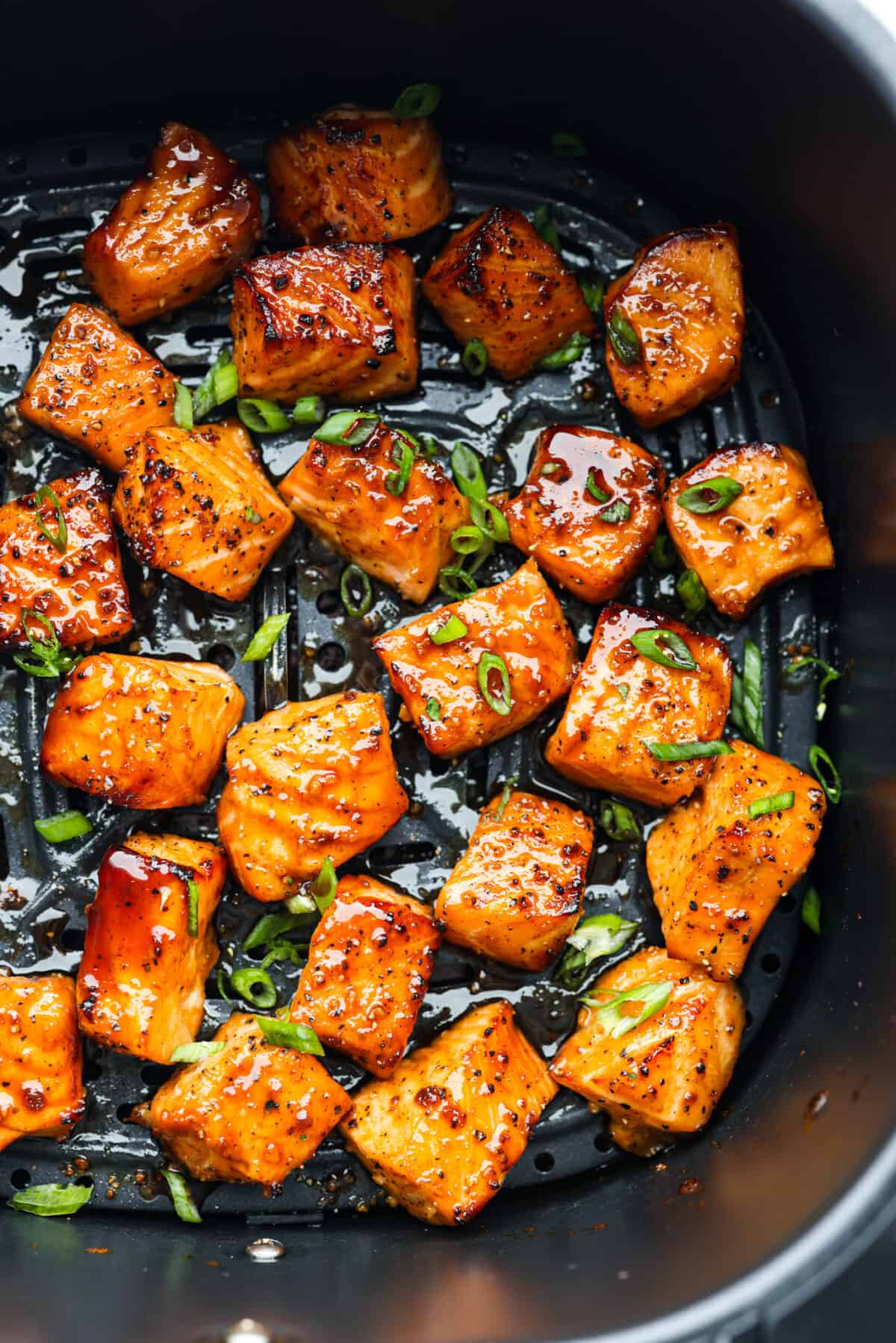 Top view of cooked salmon bites in the air fryer garnished with green onions.