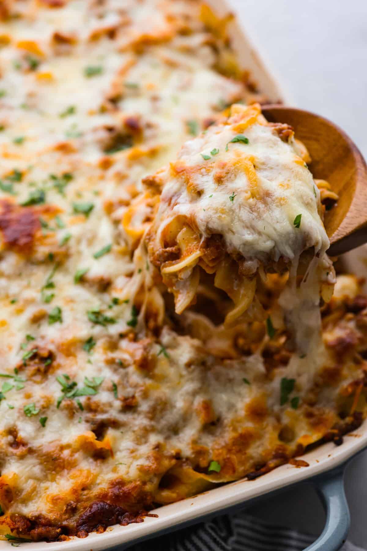 A cheesy scoop of sour cream noodle bake being pulled up with a wooden spoon.