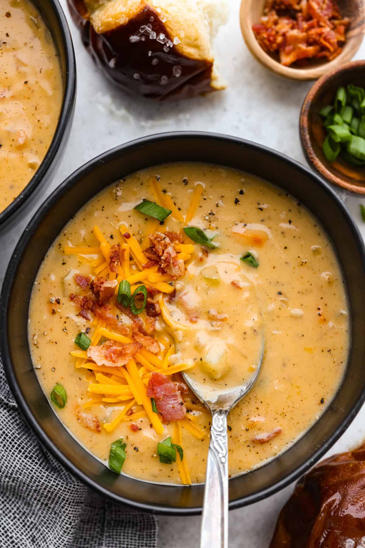 Top-down view of beer cheese soup in a black bowl, topped with shredded cheese, bacon bits, and chopped green onions.