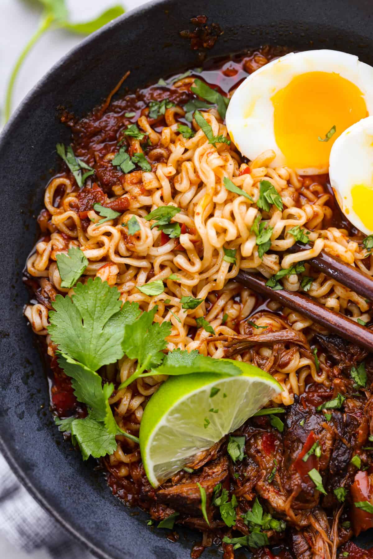 Closeup of noodles topped with cilantro and a lime wedge.