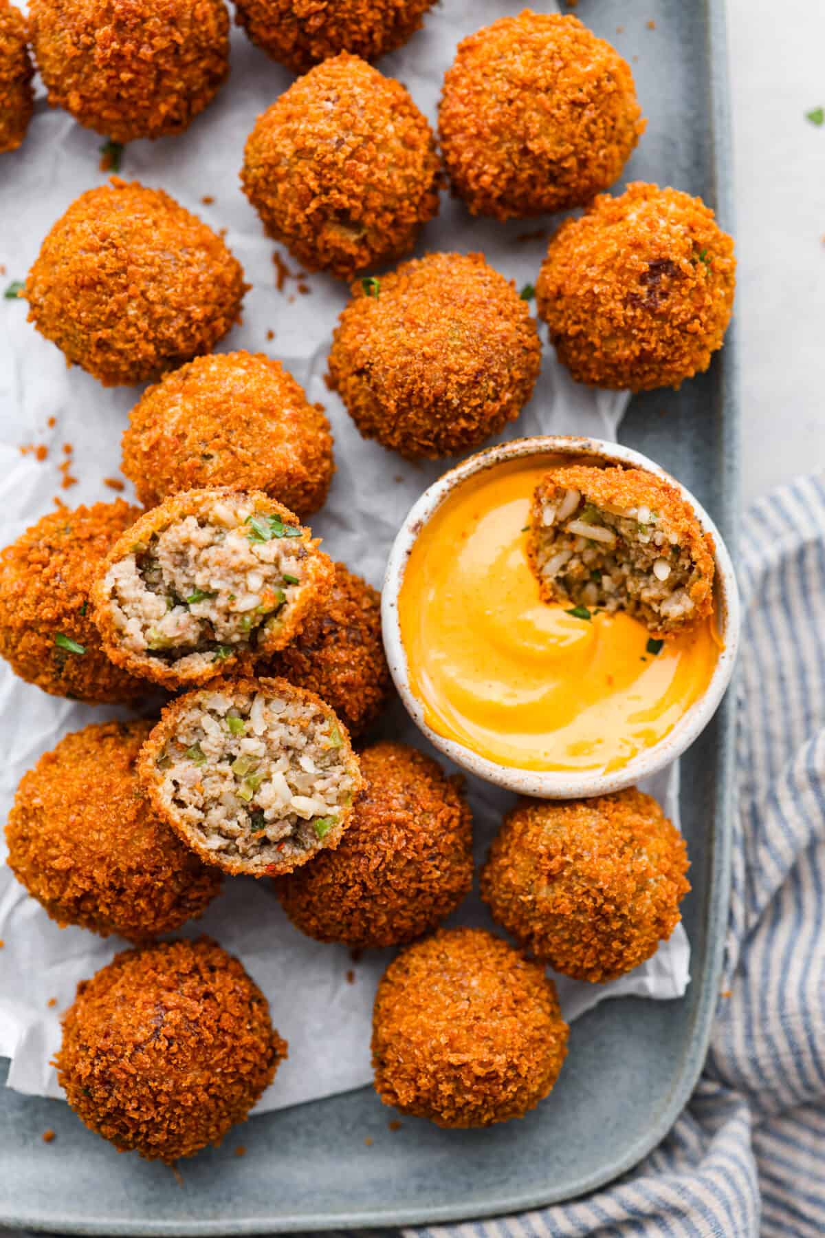 Overhead shot of boudin balls on a serving platter with half of one dipped in sauce. 