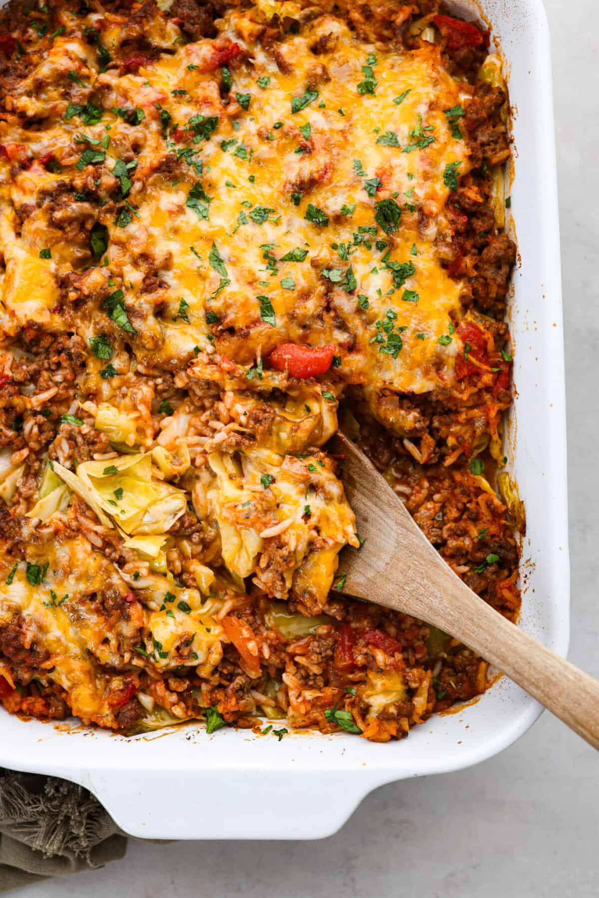 Top view of a wood serving spoon in the casserole dish of cabbage roll casserole.