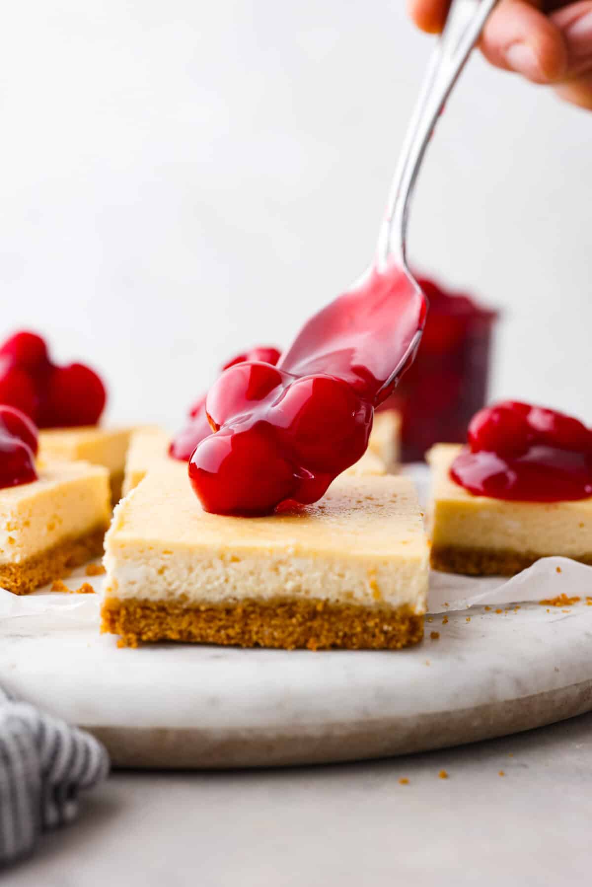 The cherry pie filling being added to a cheesecake bar.