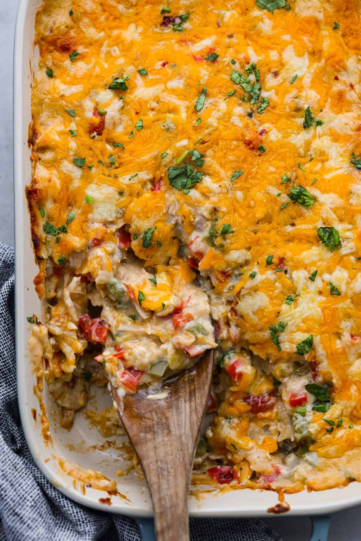 Top view of a wooden serving spoon sitting in the dish of king ranch casserole.