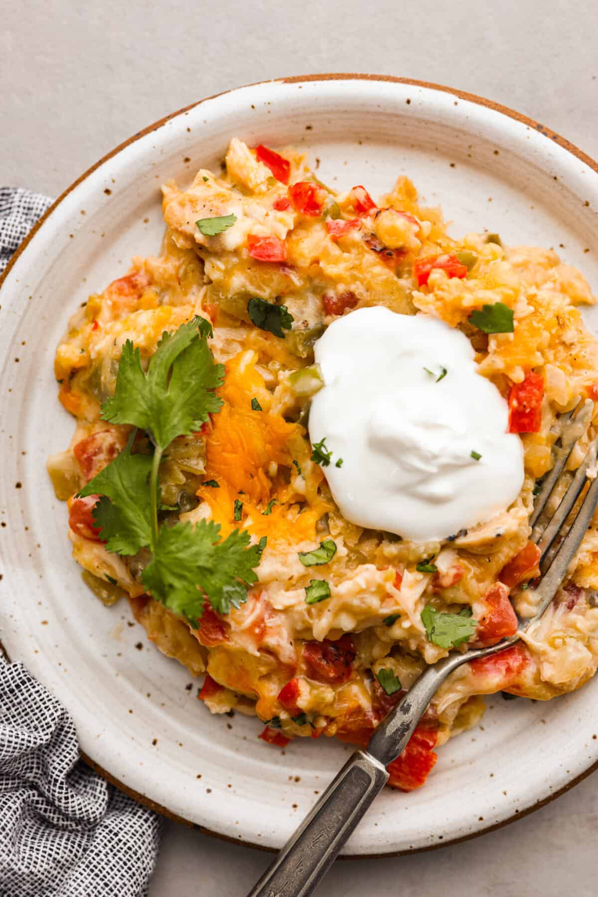 Top view of a serving of king ranch casserole on a plate garnished with cilantro and sour cream.