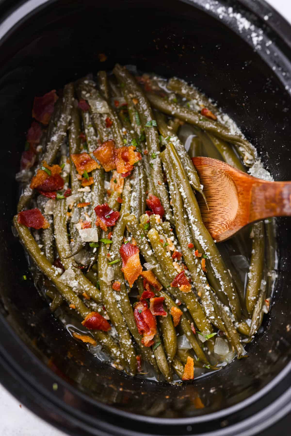 Green beans in a slow cooker, topped with cheese and bacon.