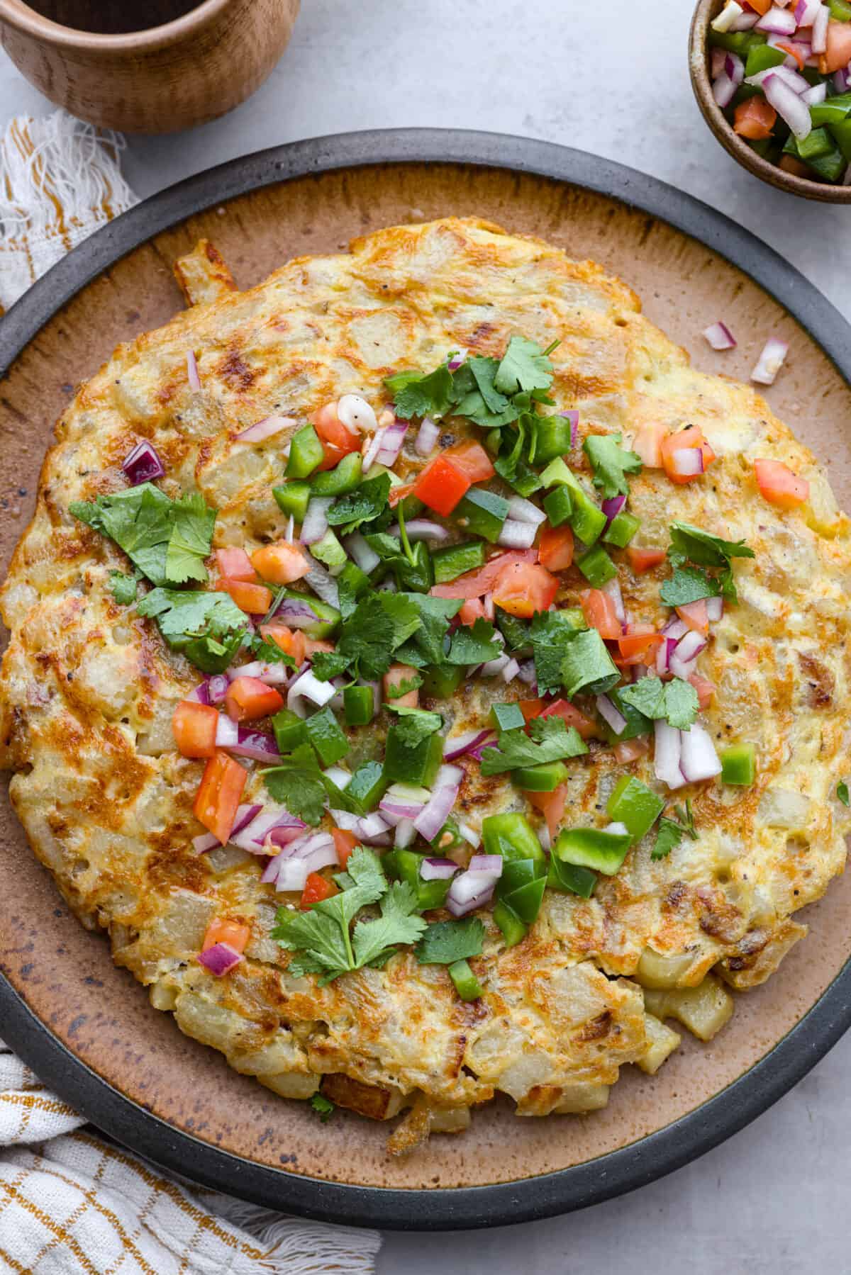 Top view of Spanish tortilla on a large plate topped with salsa and cilantro.