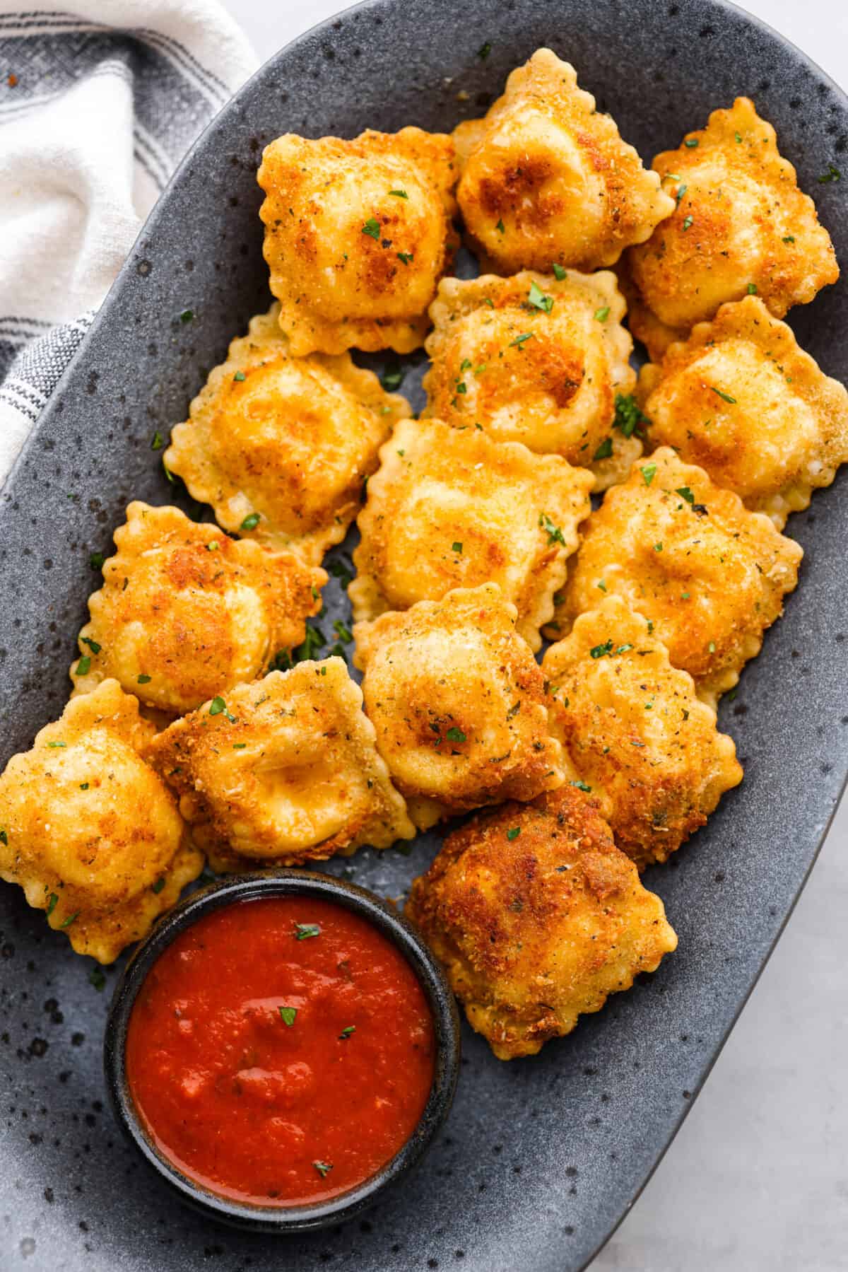 Toasted ravioli on a gray serving platter, with a side of marinara sauce.